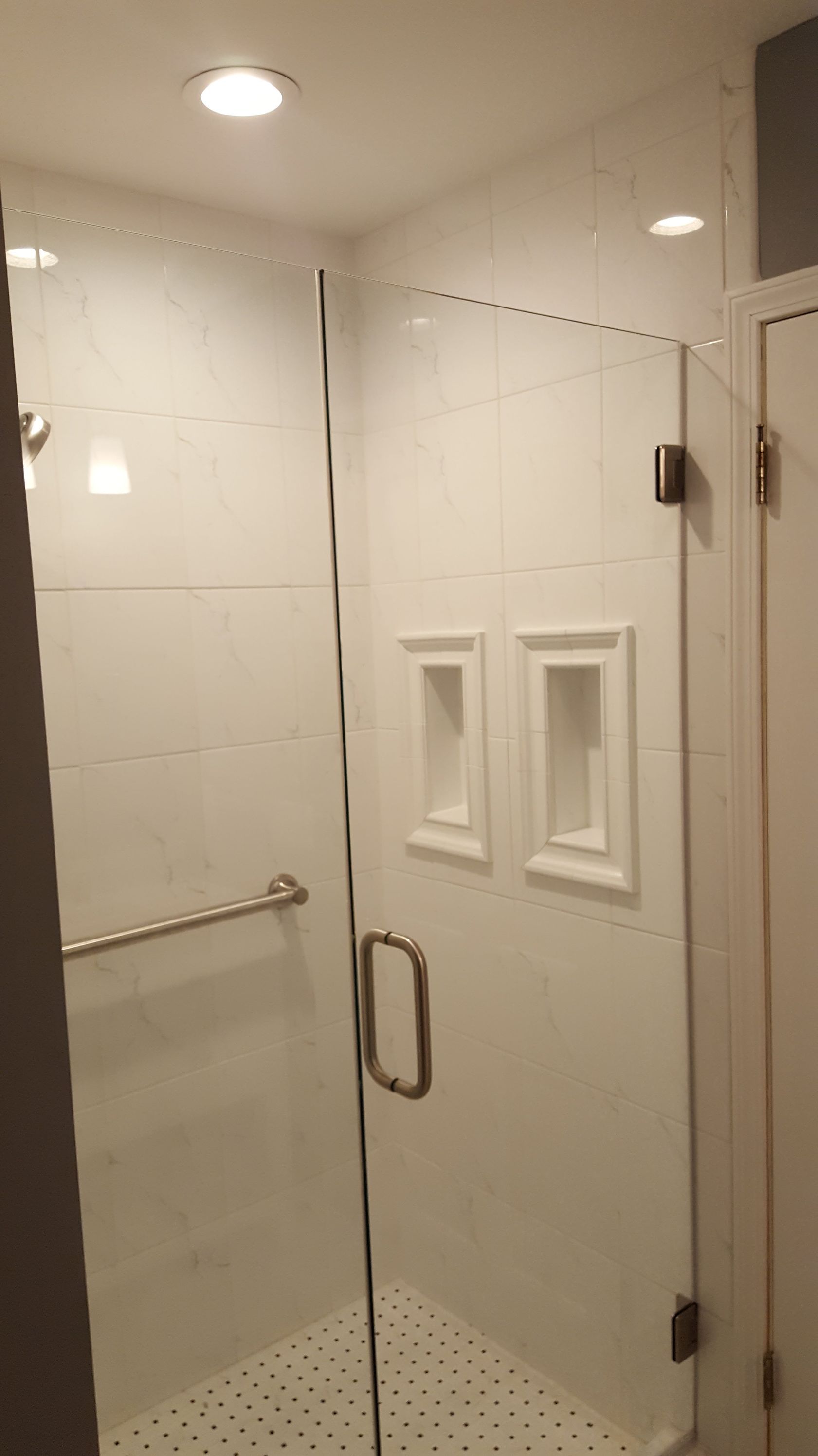 White shower stall with glass door, chrome handle, and built-in wall niches in a tiled bathroom.