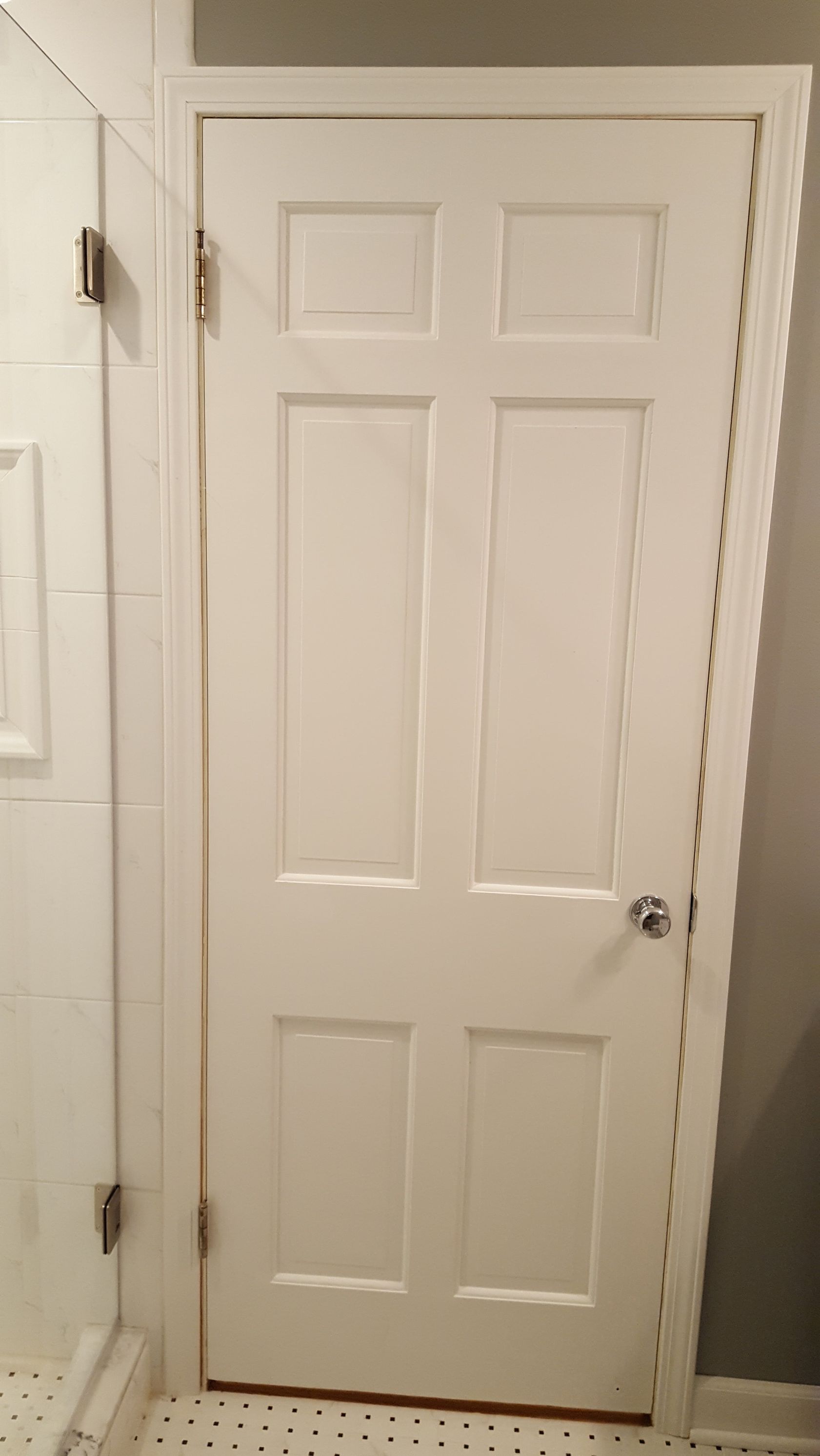 White paneled interior door with a silver knob in a bathroom-like hallway.