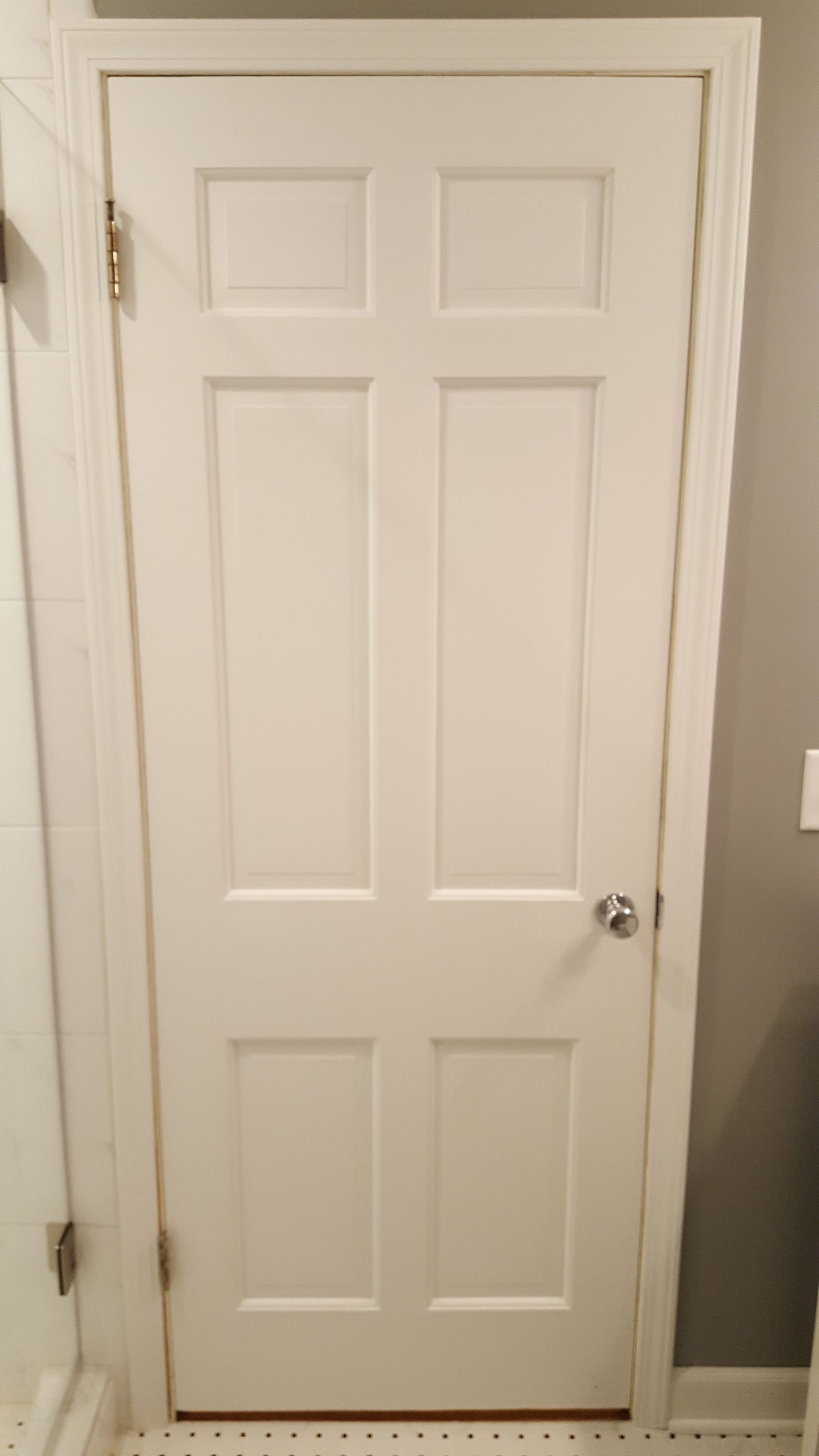 Closed white paneled interior door with brass hinges and silver knob against gray walls