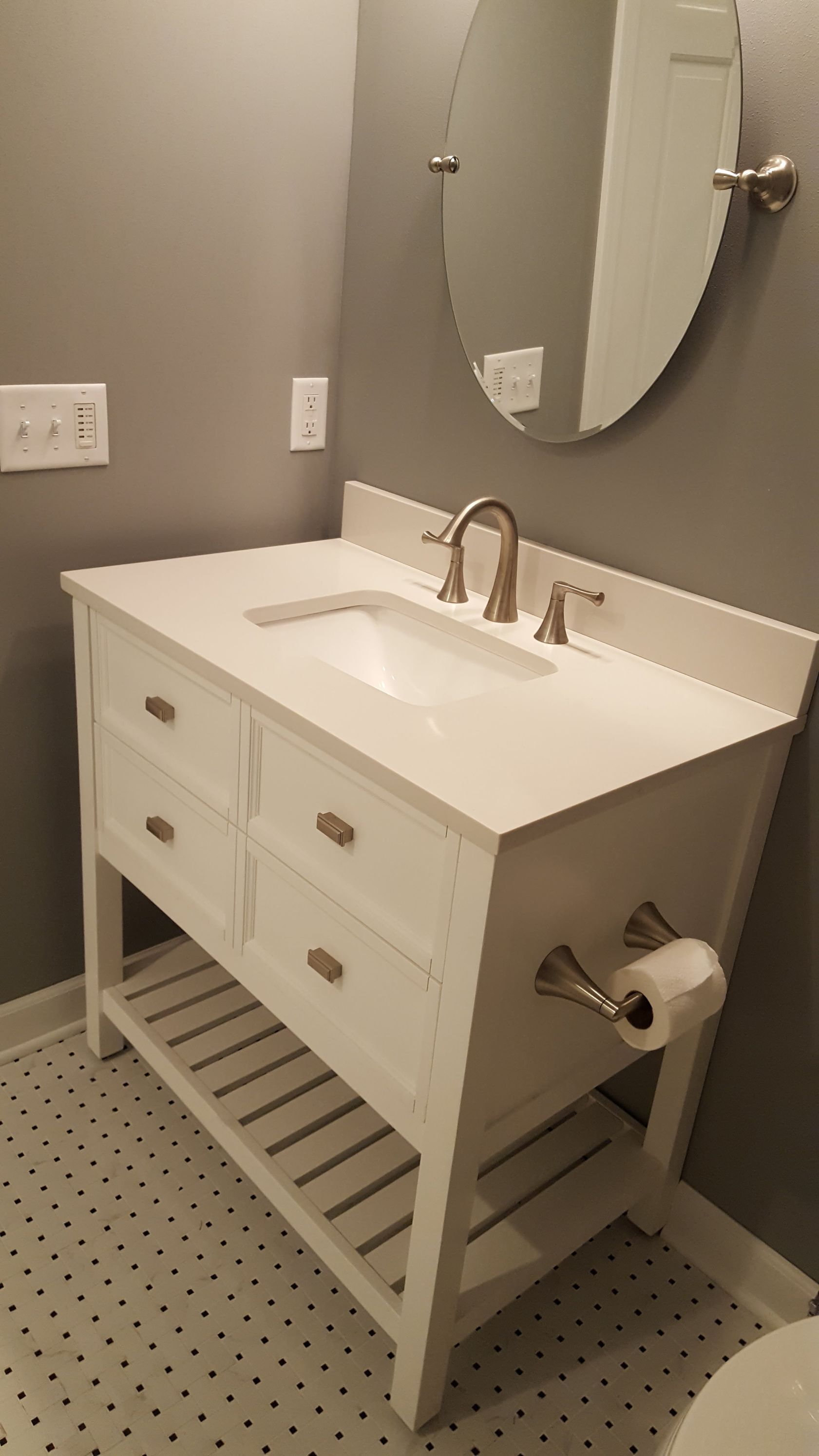 White vanity sink with mirror in a gray-tiled bathroom, with towel bars and a wall outlet.