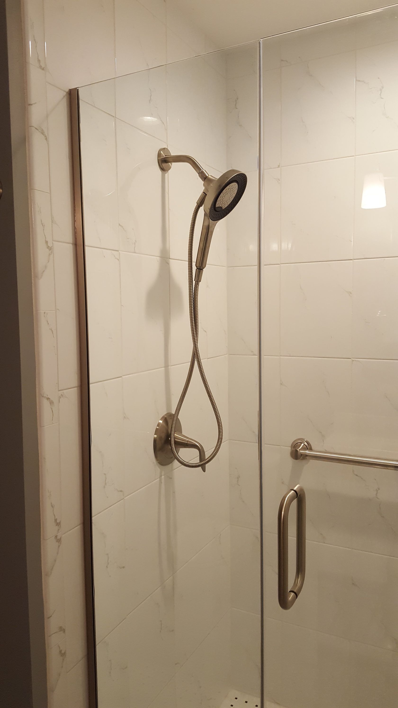 Shower stall with a handheld showerhead and chrome grab bar on white tiled walls.