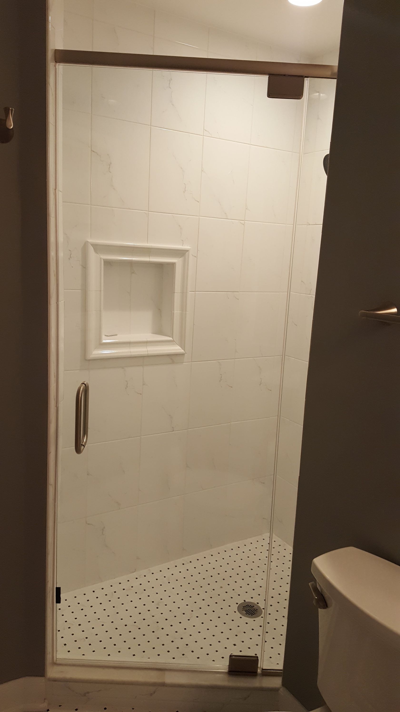 Glass shower door in a bathroom, with white tile walls and a built-in shower shelf.