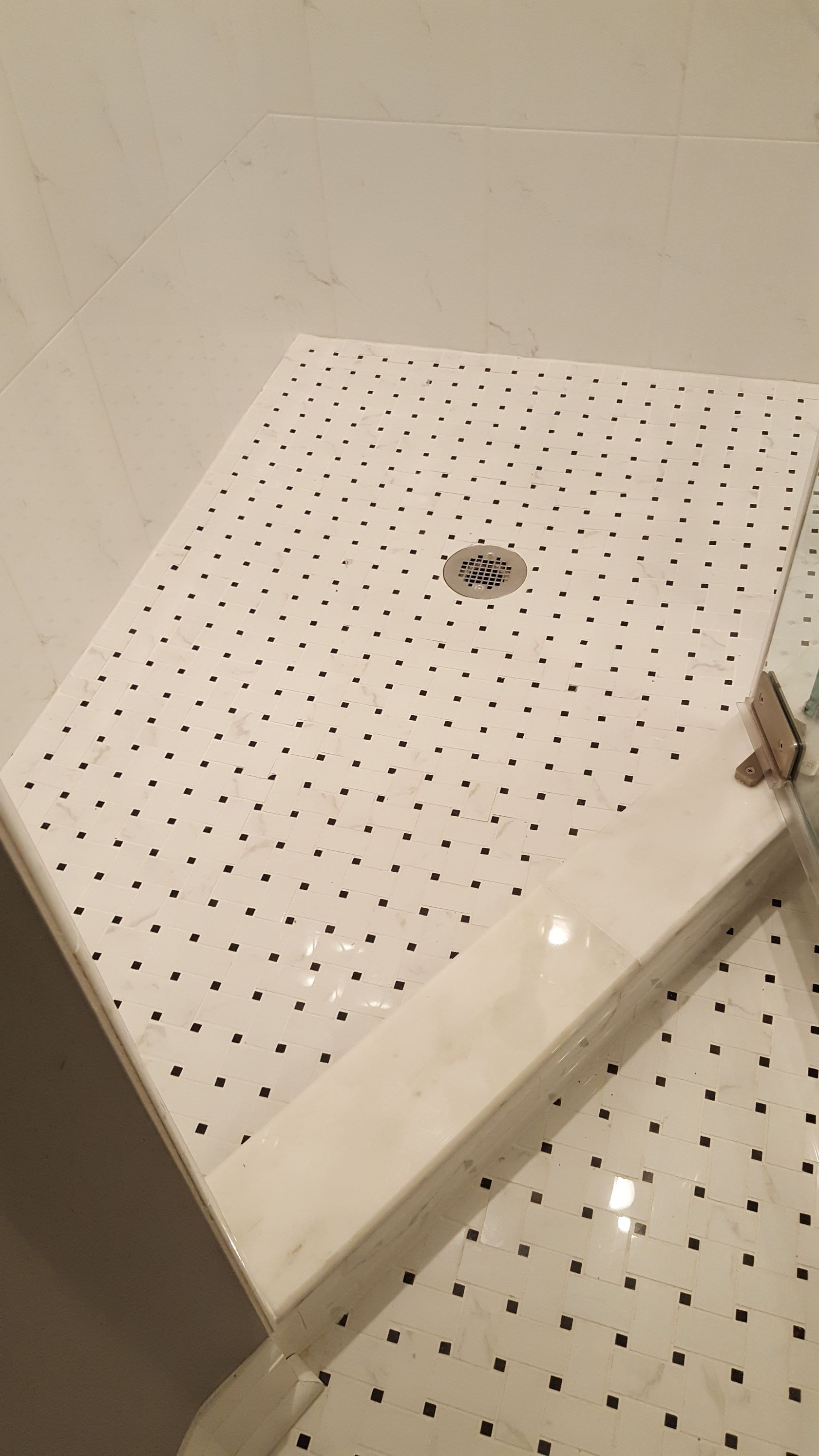 Small white tiled shower stall with a central drain and built-in bench.