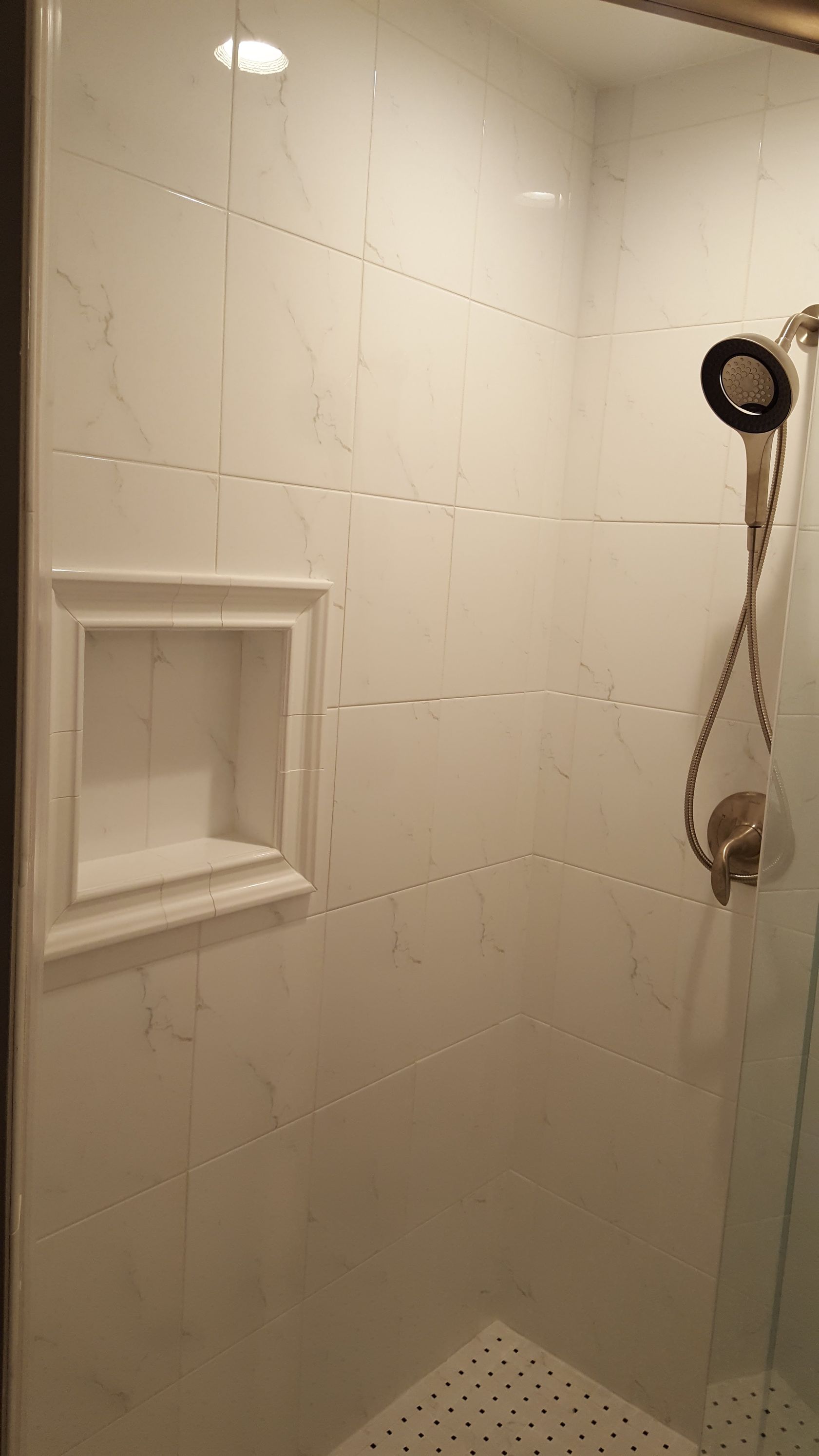 Tiled shower stall with a built-in shelf, glass door, and handheld showerhead.