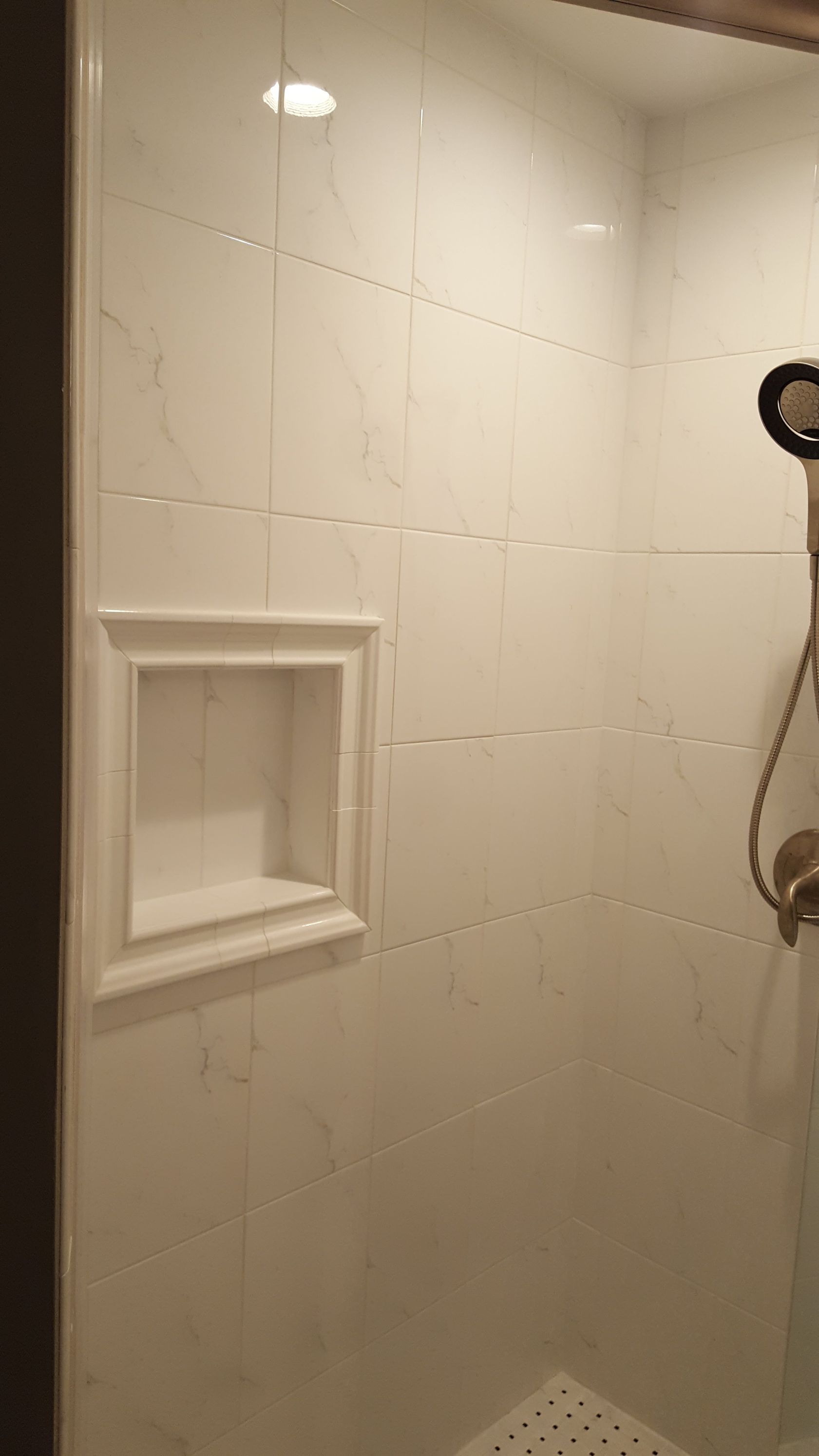White-tiled shower stall with built-in shelf and handheld showerhead.
