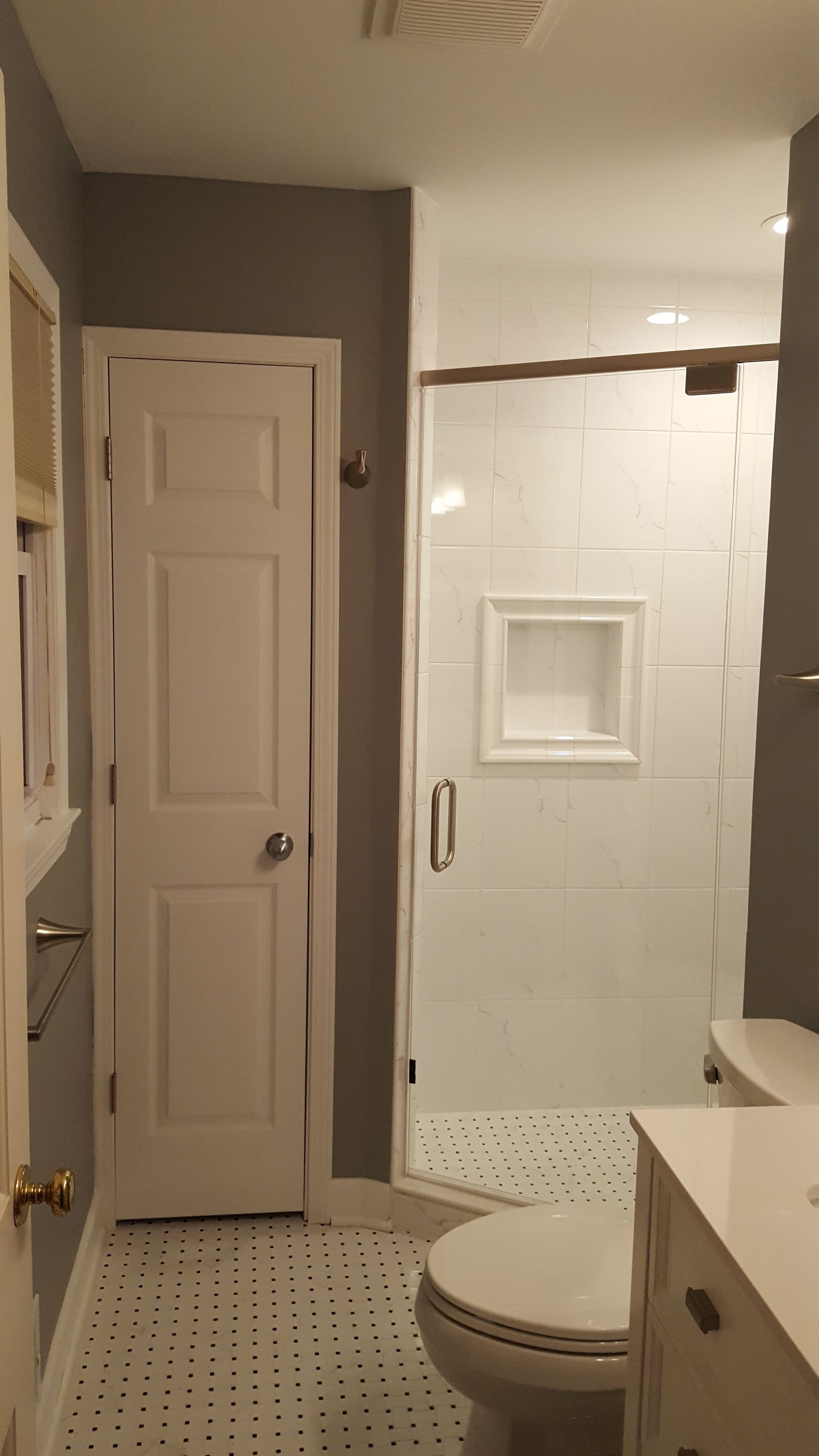 Small bathroom with white tile shower, toilet, vanity, and closed door.