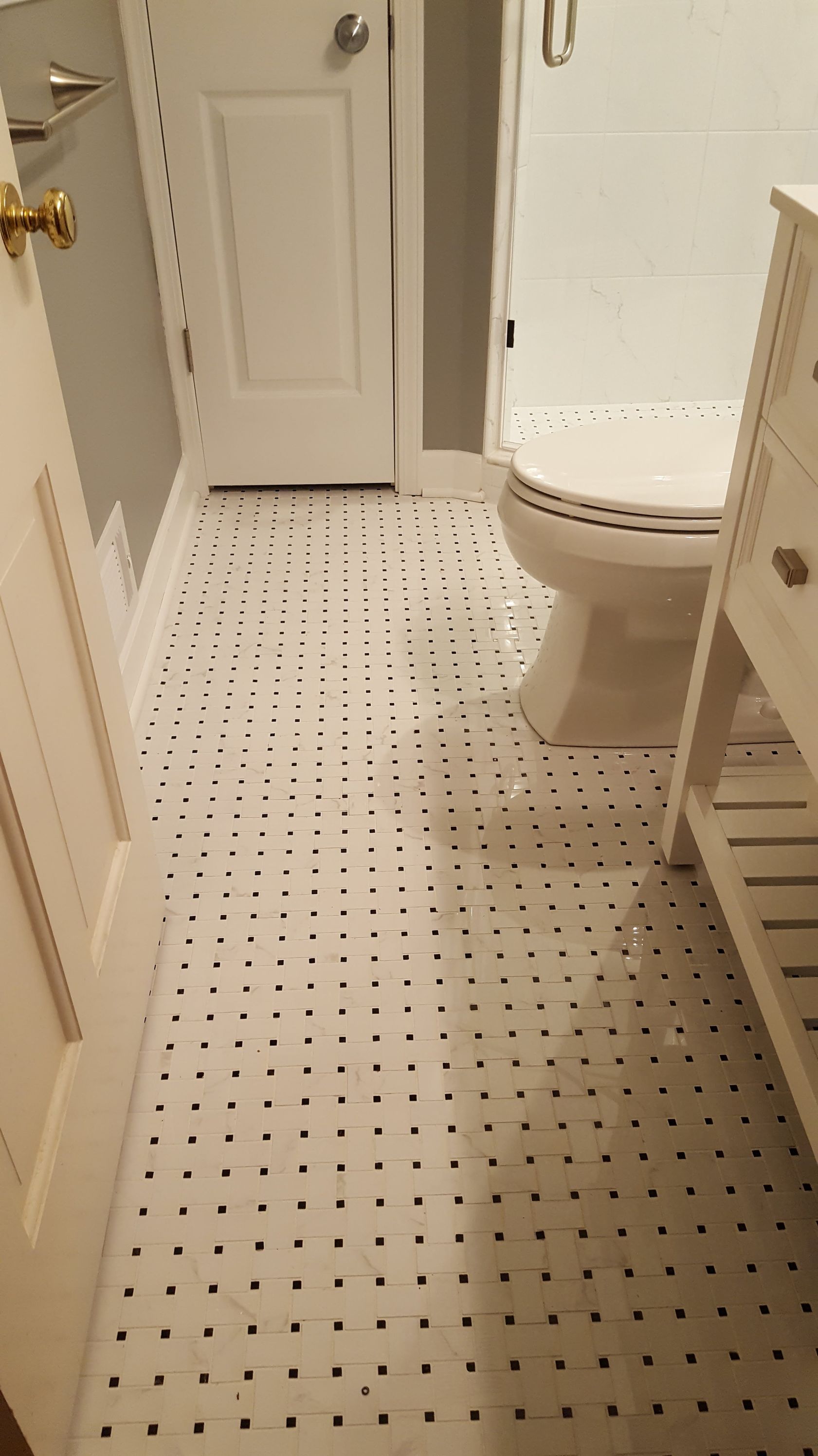 Small bathroom with white tiled floor, toilet on right, sink cabinet on left, and closed door ahead.
