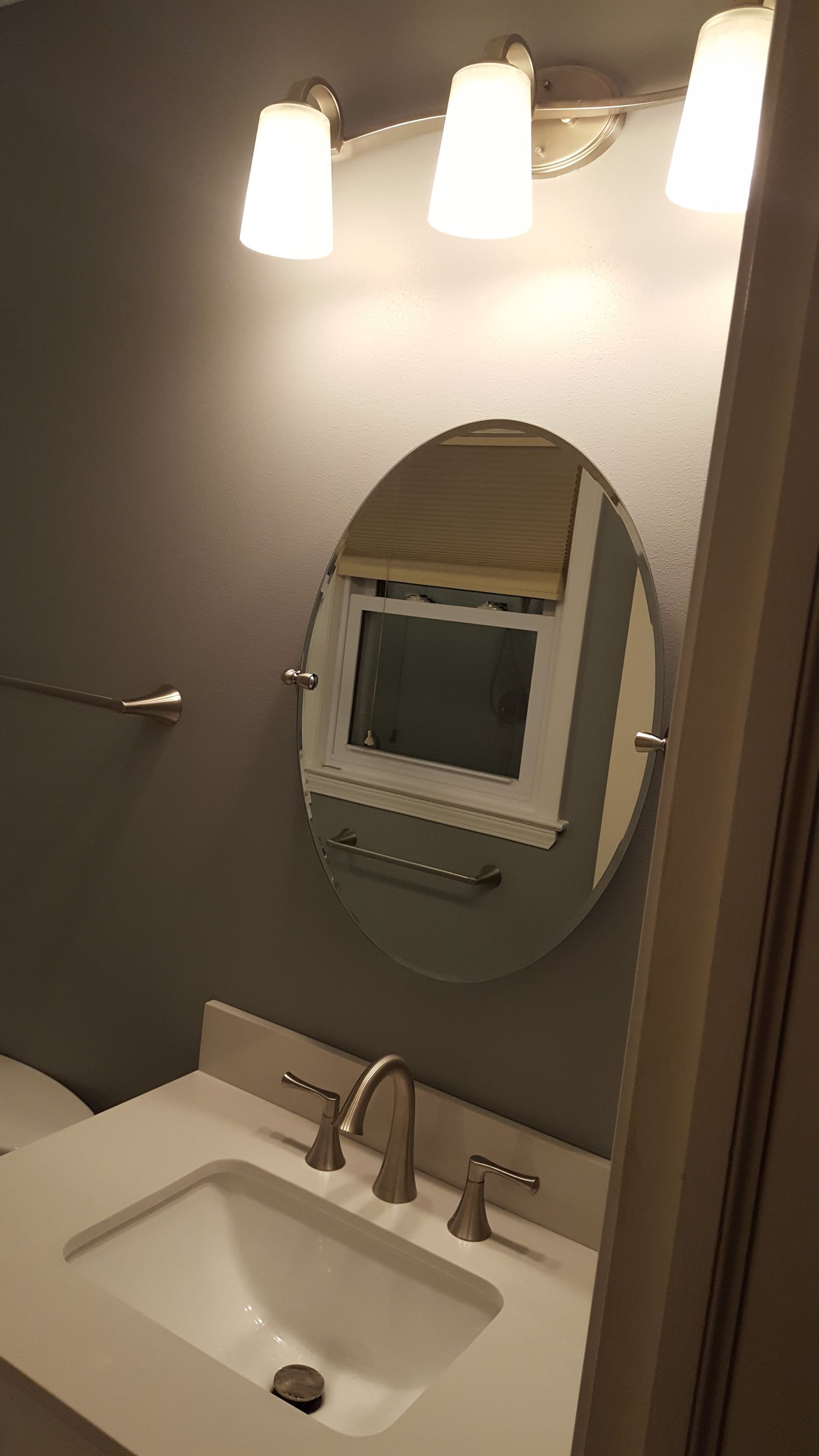 Bathroom sink with oval mirror and three lights above a white vanity.