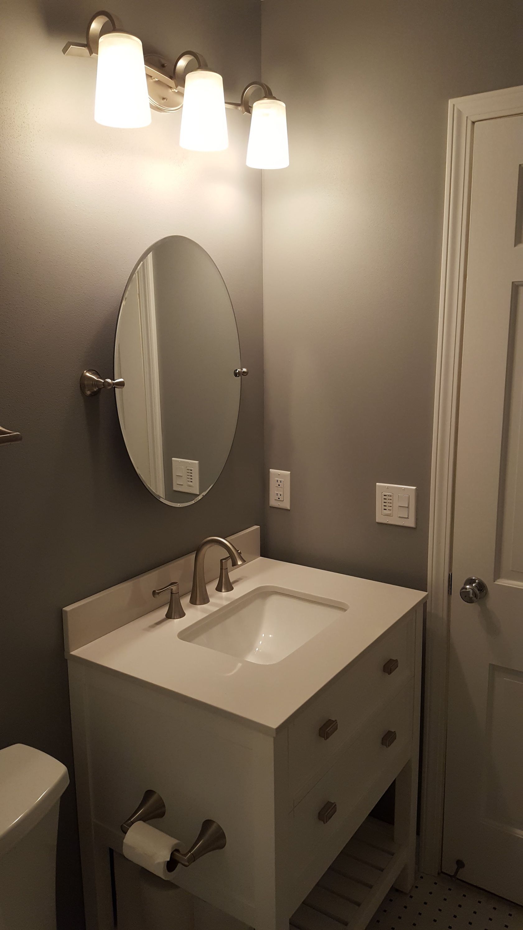 Small bathroom with a white vanity, oval mirror, three vanity lights, and a shower curtain on the right.