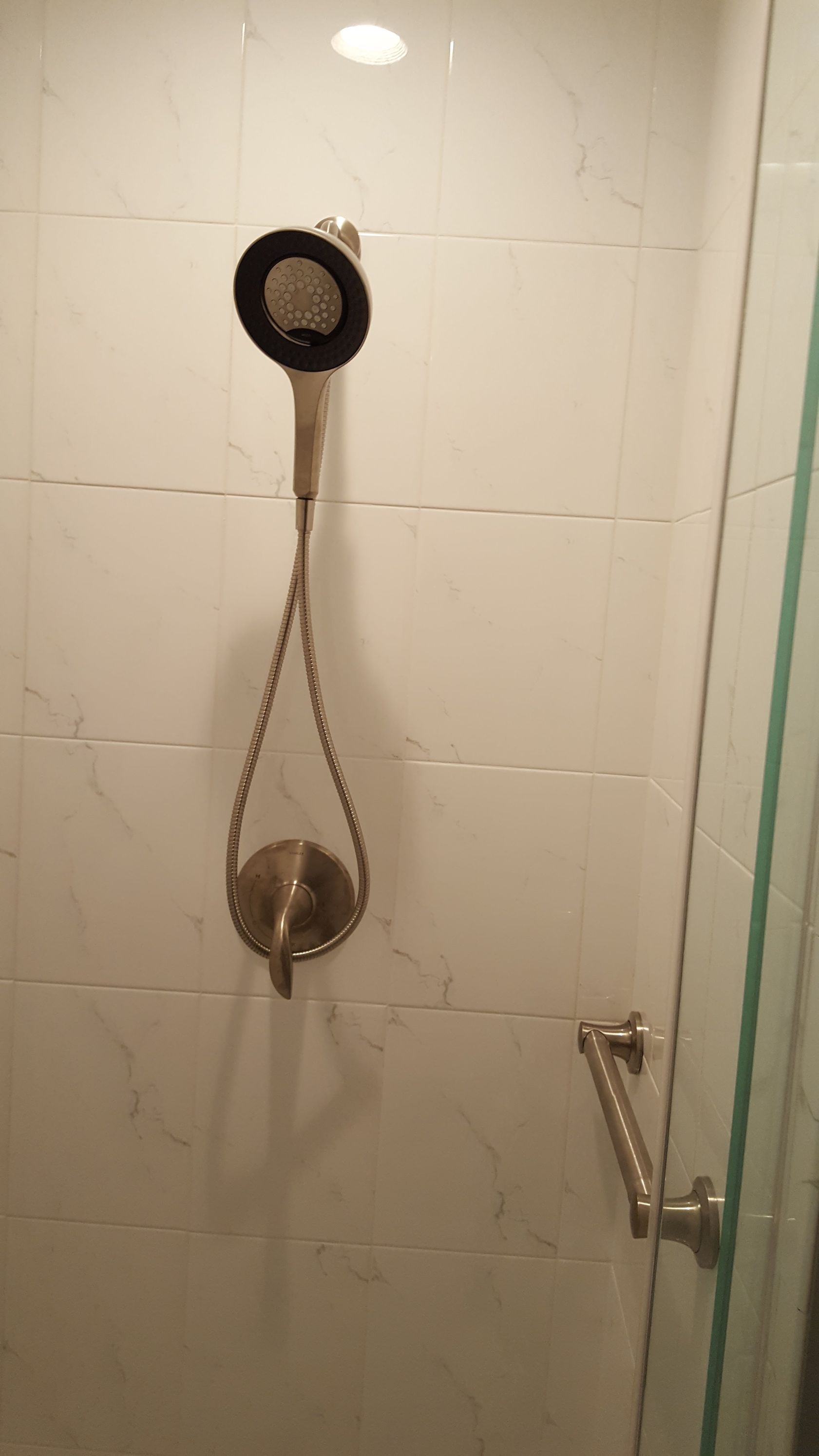 Shower stall with handheld showerhead, hose, and glass door in a tiled bathroom