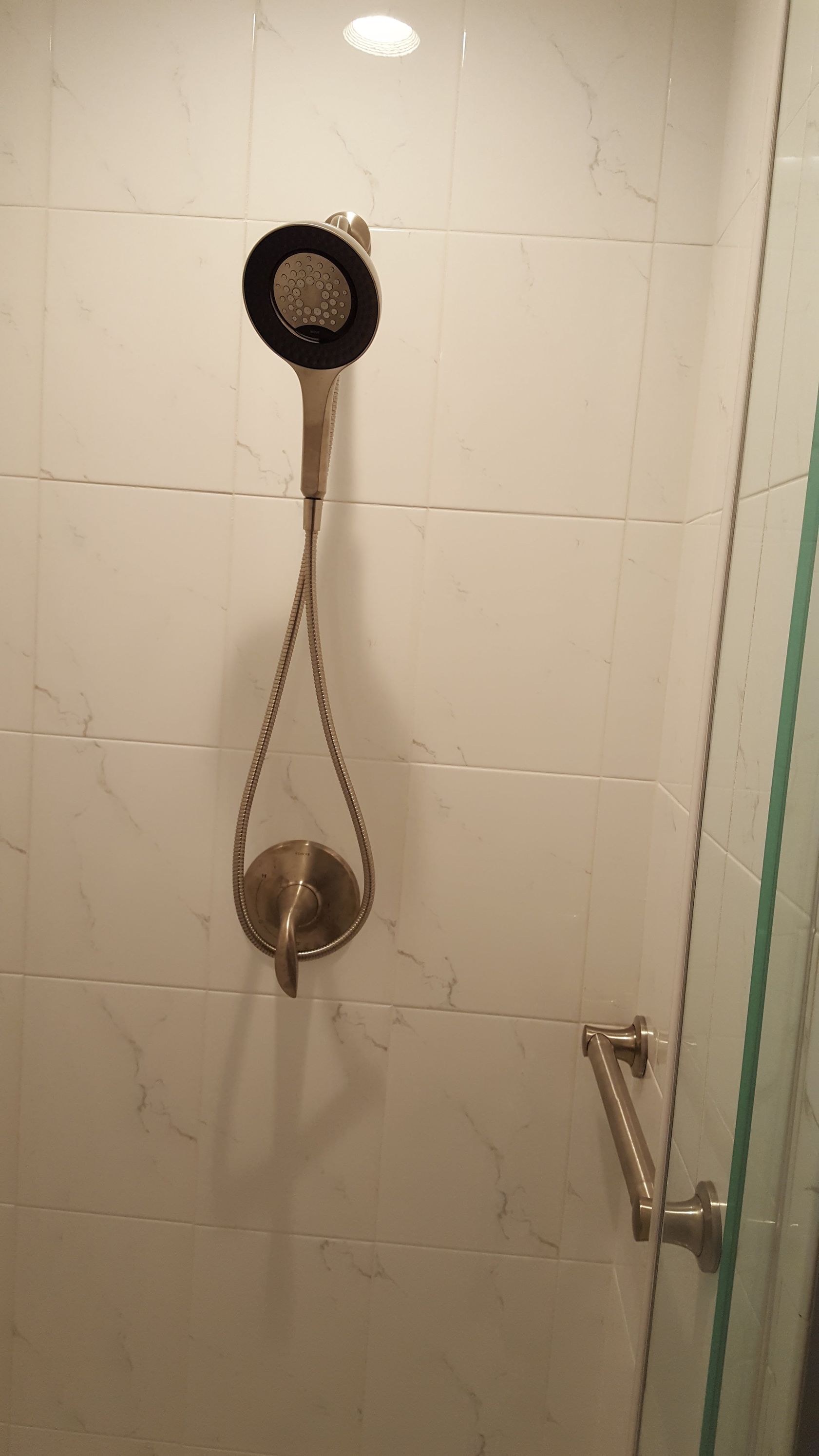 Shower wall with handheld showerhead, hose, and control knob in a tiled bathroom