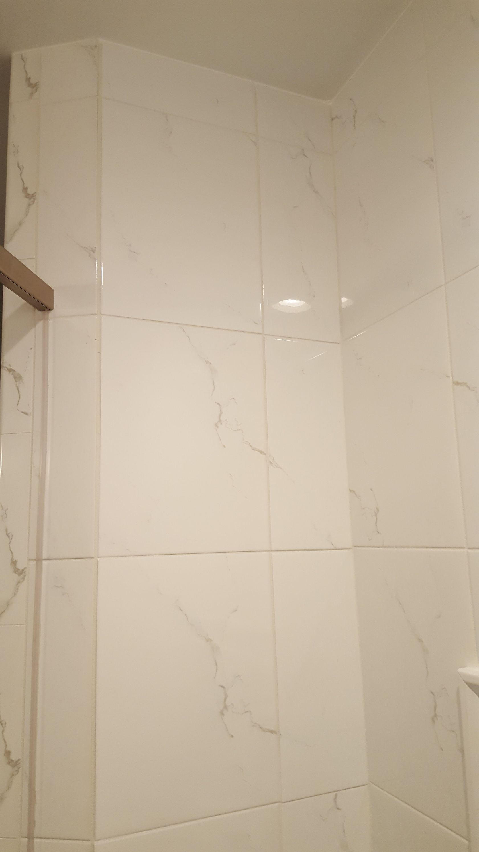 White tiled shower wall with subtle gray veining and a chrome shower fixture on the right.