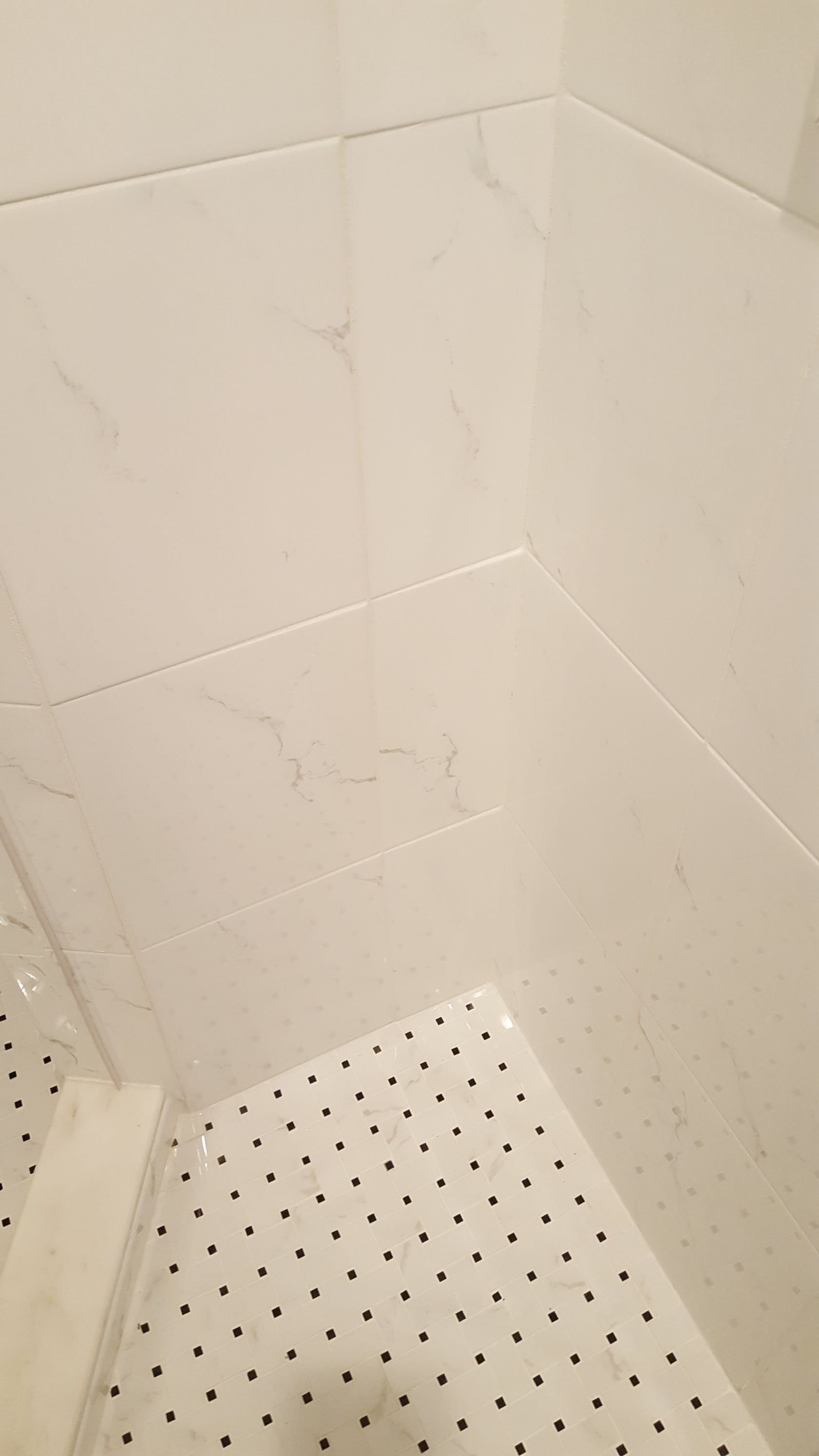 Corner of a white-tiled shower with a perforated white shower floor.