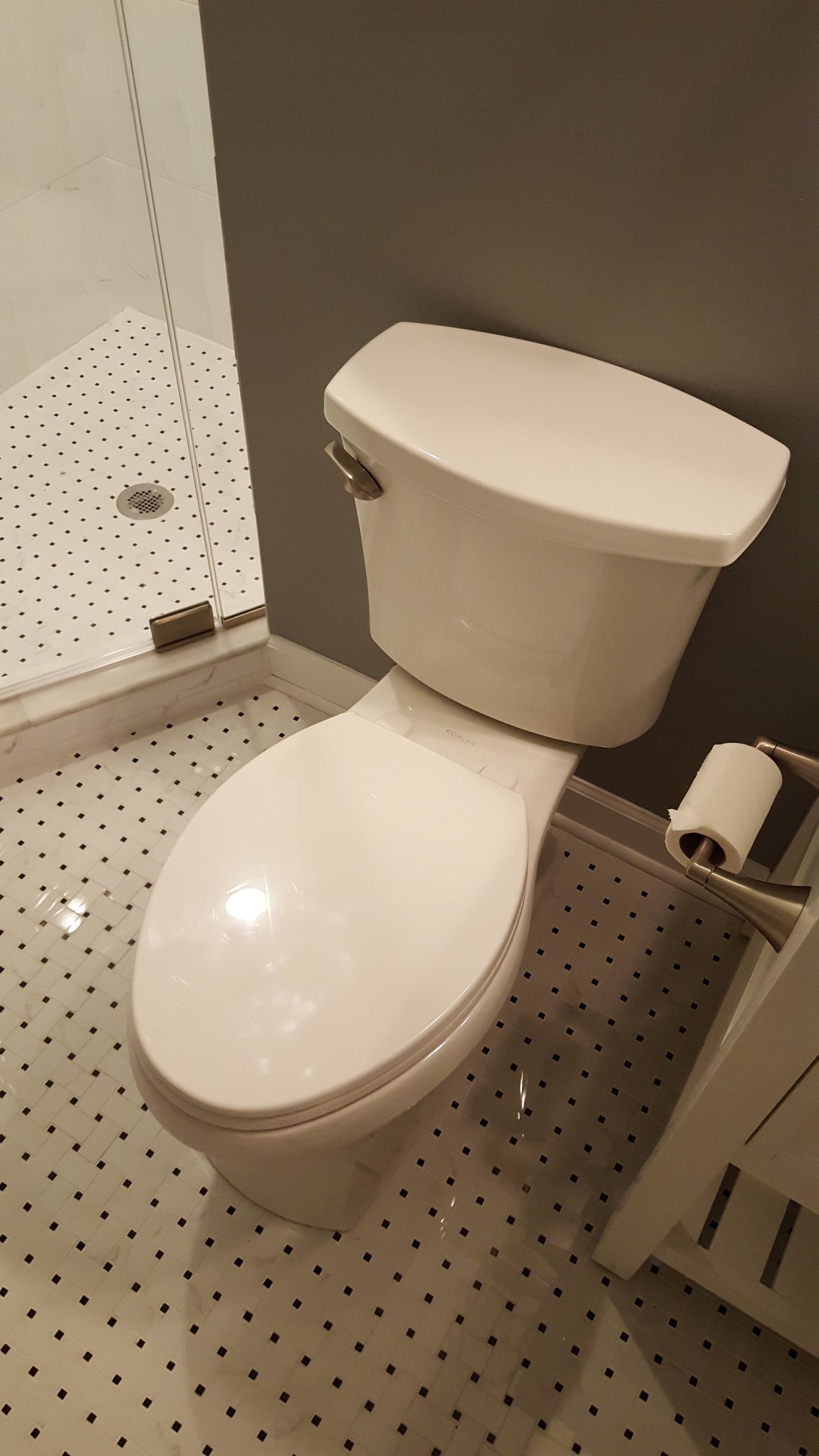 White toilet in a small tiled bathroom with a roll of toilet paper on the wall.