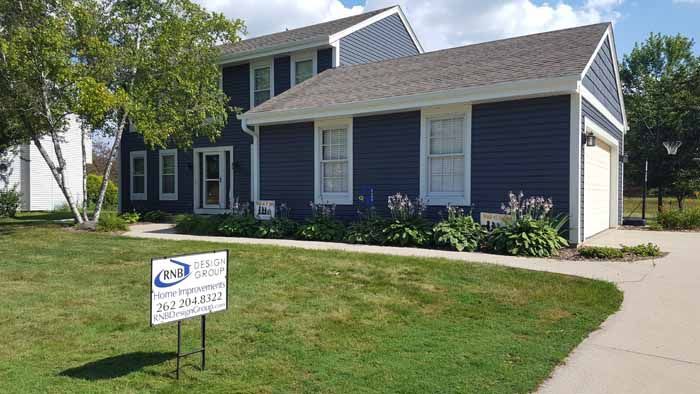 Blue house with white trim and a real estate sign on a grassy lawn beside a driveway