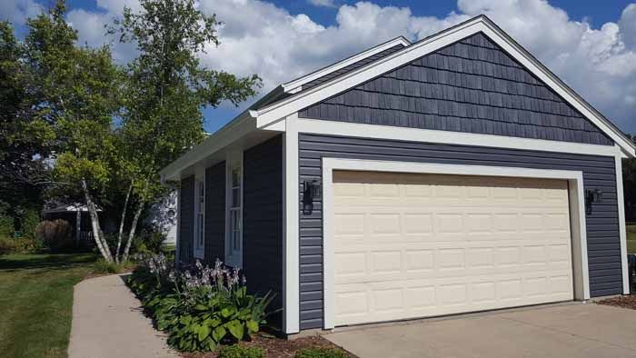 Blue-gray house with white trim and a beige garage door beside a driveway and trees