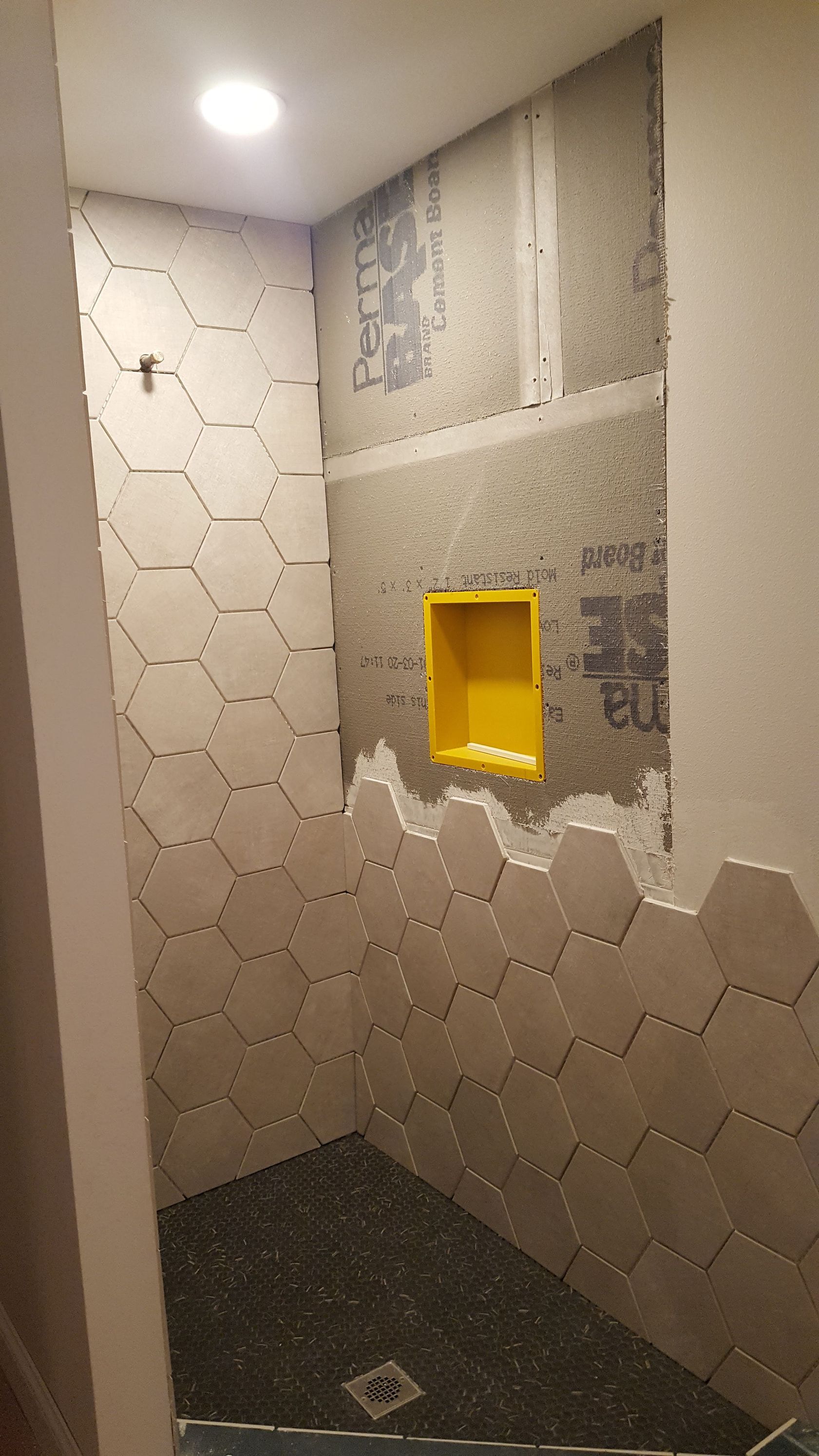 Small shower stall with white hex tile walls, a yellow recessed shelf, and dark mosaic floor.