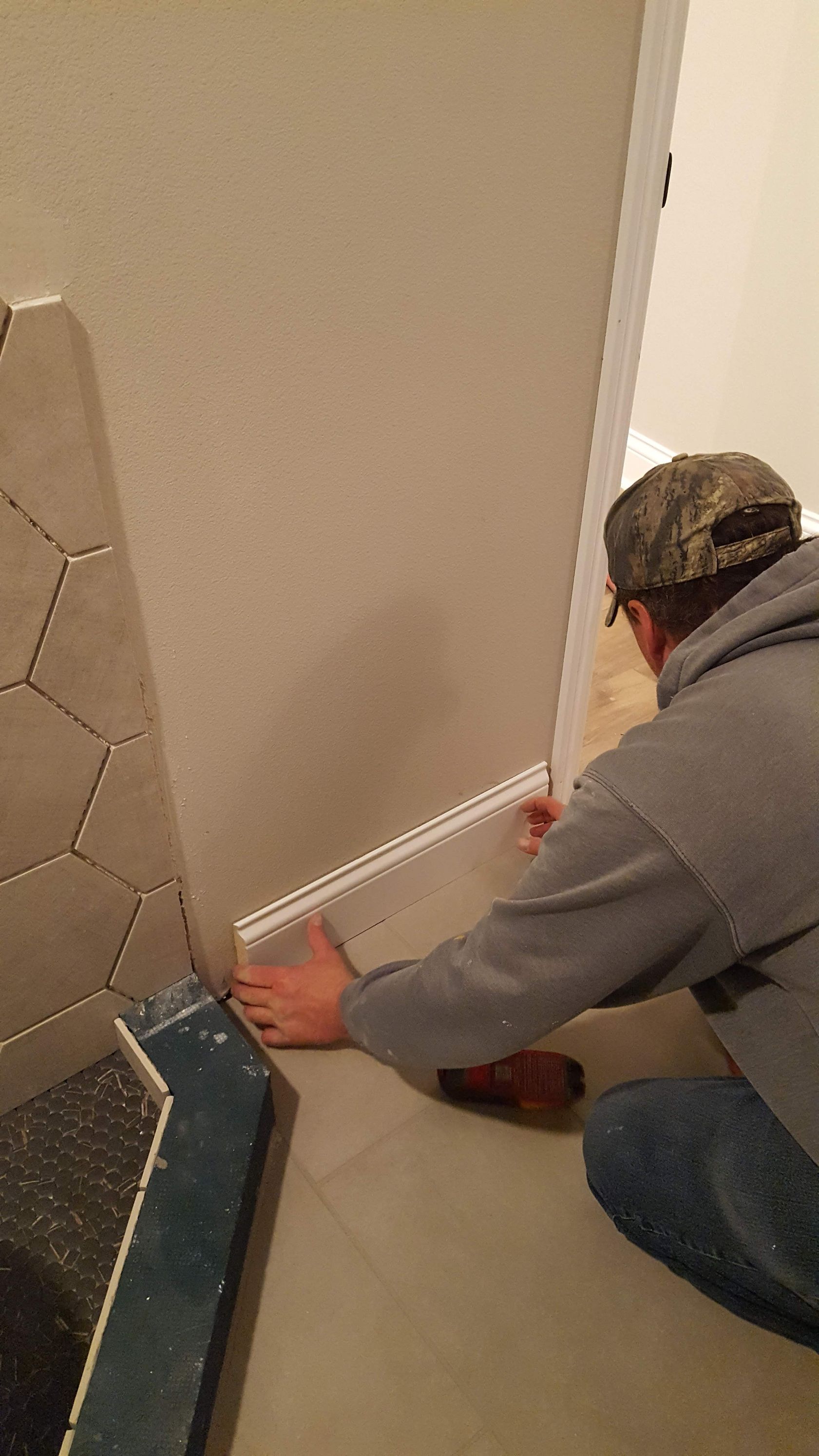 Person kneeling on a hallway floor measuring the baseboard near a wall and mirror.