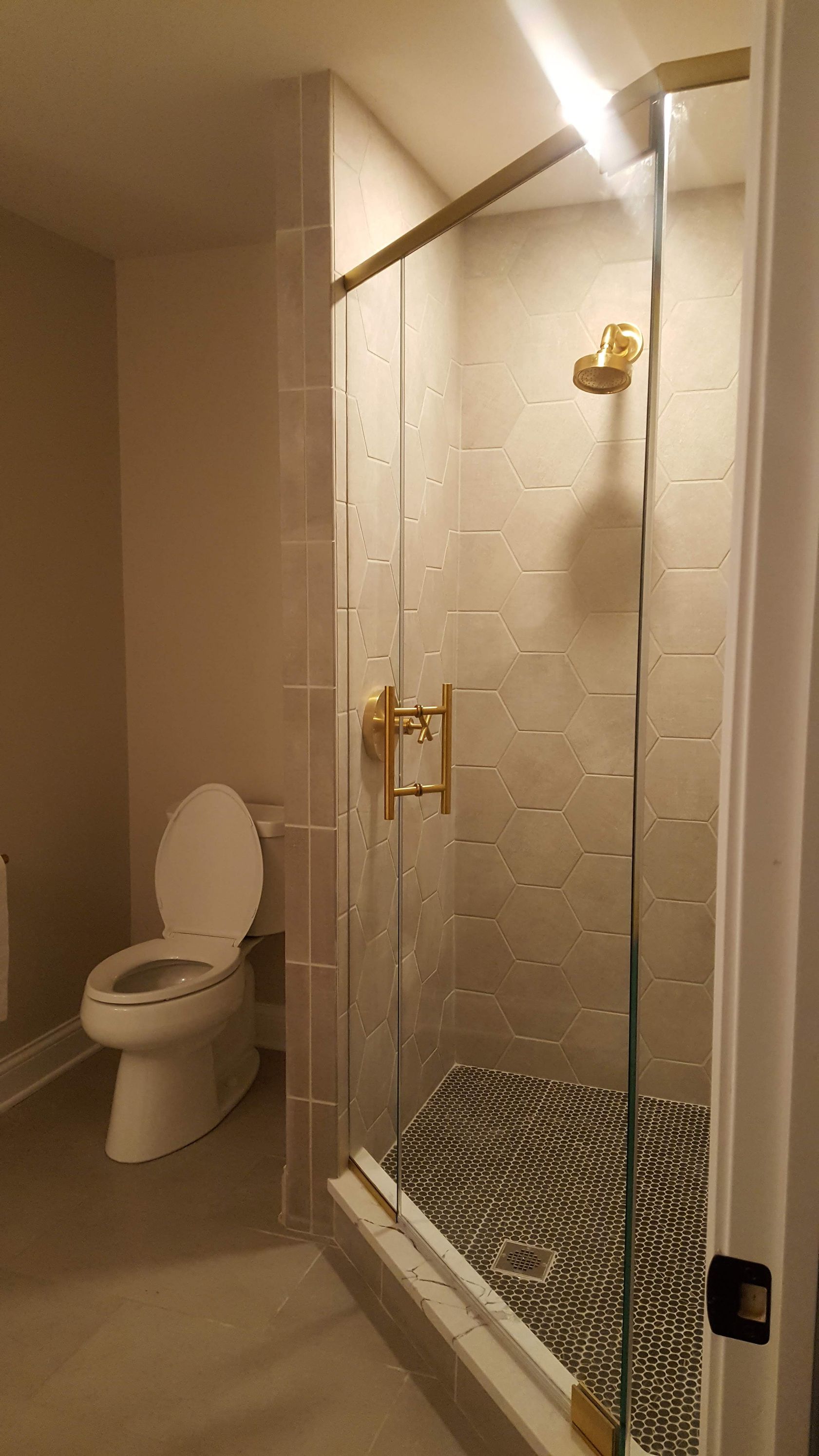 Bathroom with toilet and glass shower enclosure, white tile walls, and pebble shower floor.