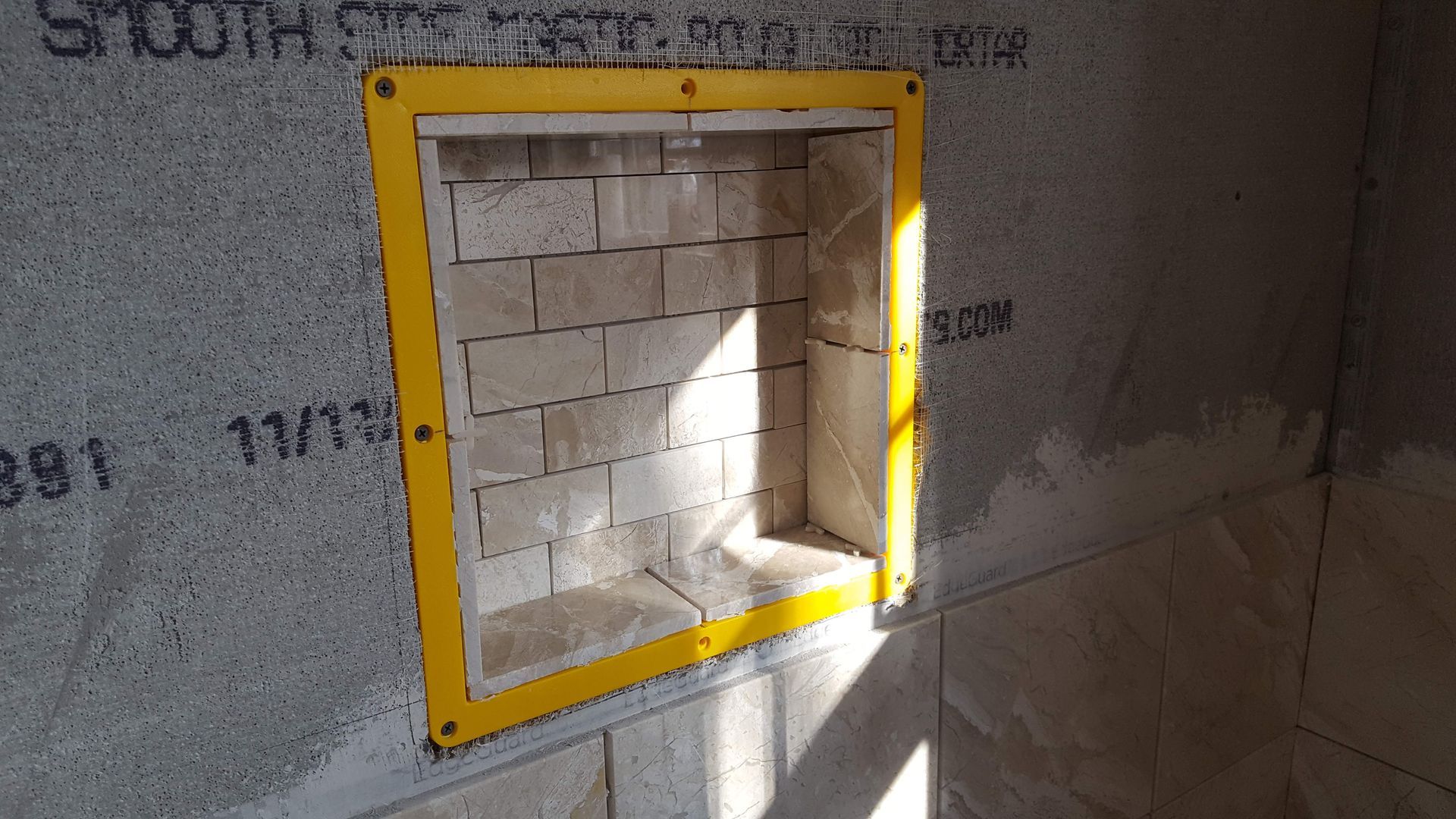 Yellow-framed wall niche with white brick interior, lit by sunlight on a gray wall
