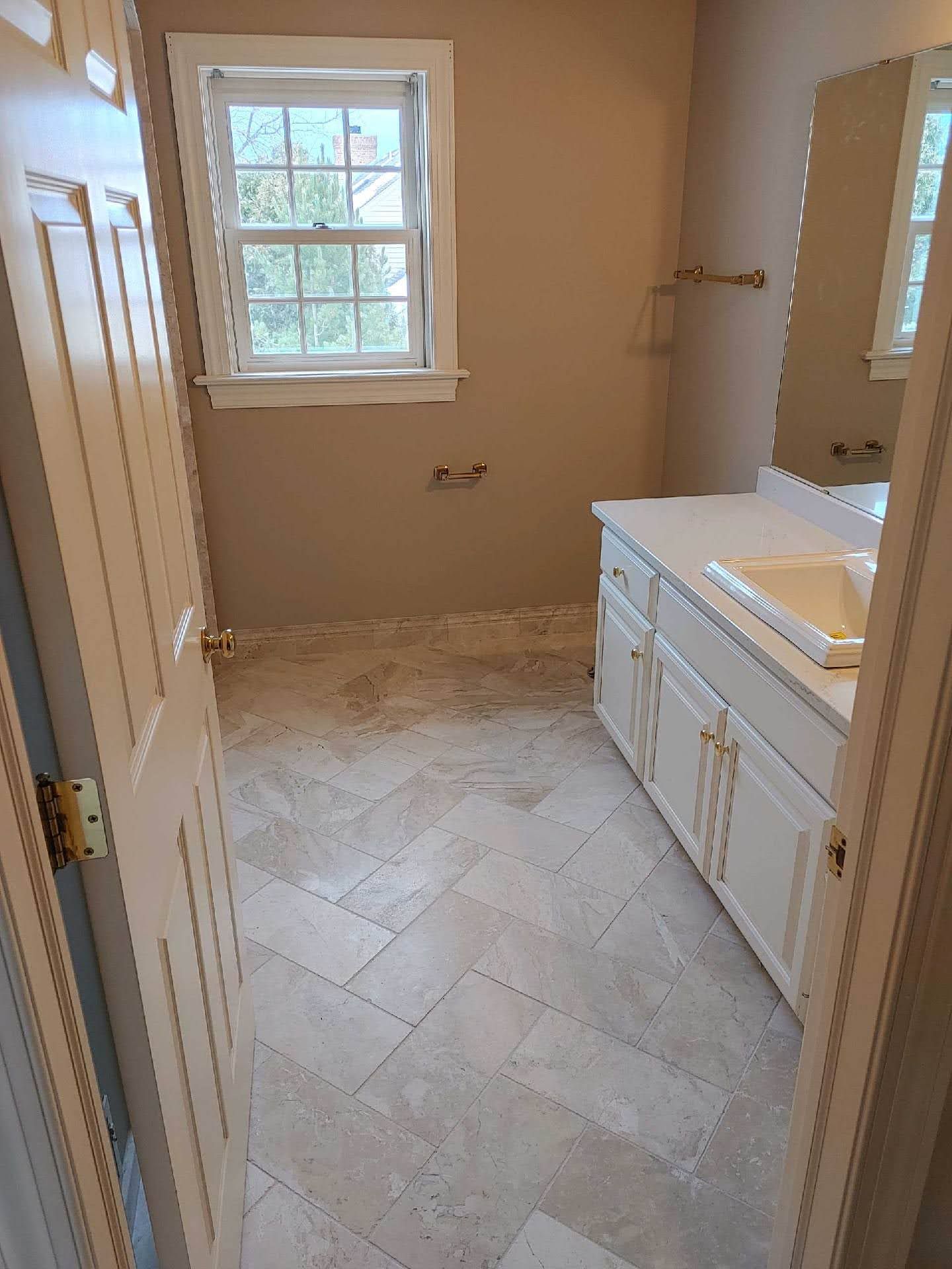 Empty bathroom with a window, white vanity, and beige tile floor.