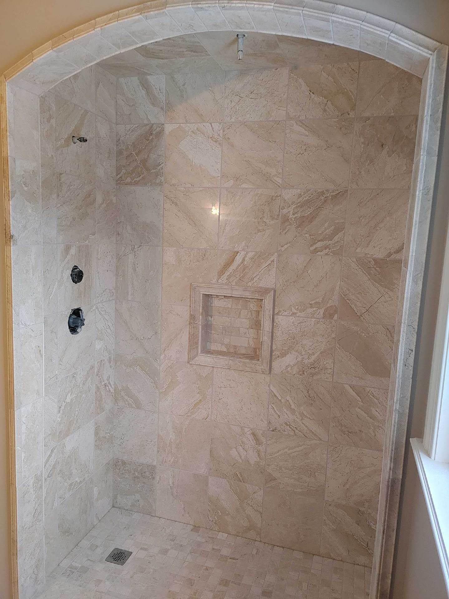 Stone-tiled walk-in shower with arched opening, built-in niche, and two wall fixtures