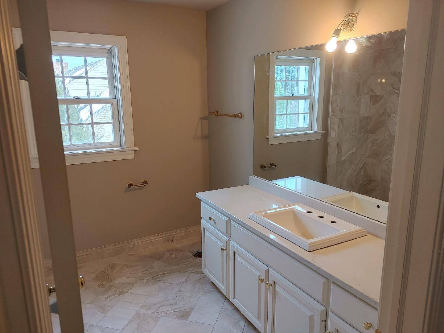 Bathroom with vanity, large mirror, sink, window, and tiled shower in soft beige tones
