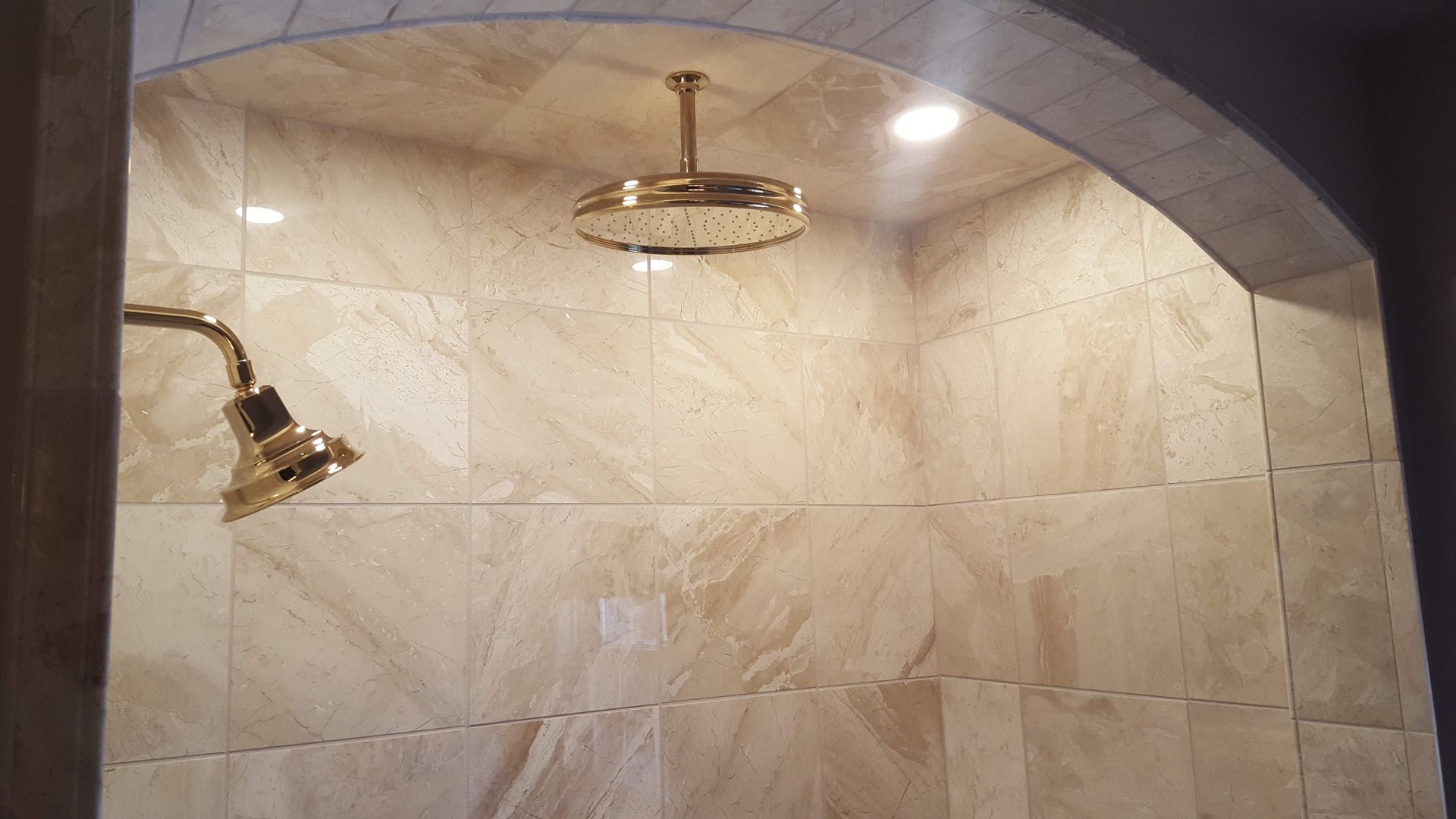 Stone-tiled shower with two gold showerheads under an arched ceiling