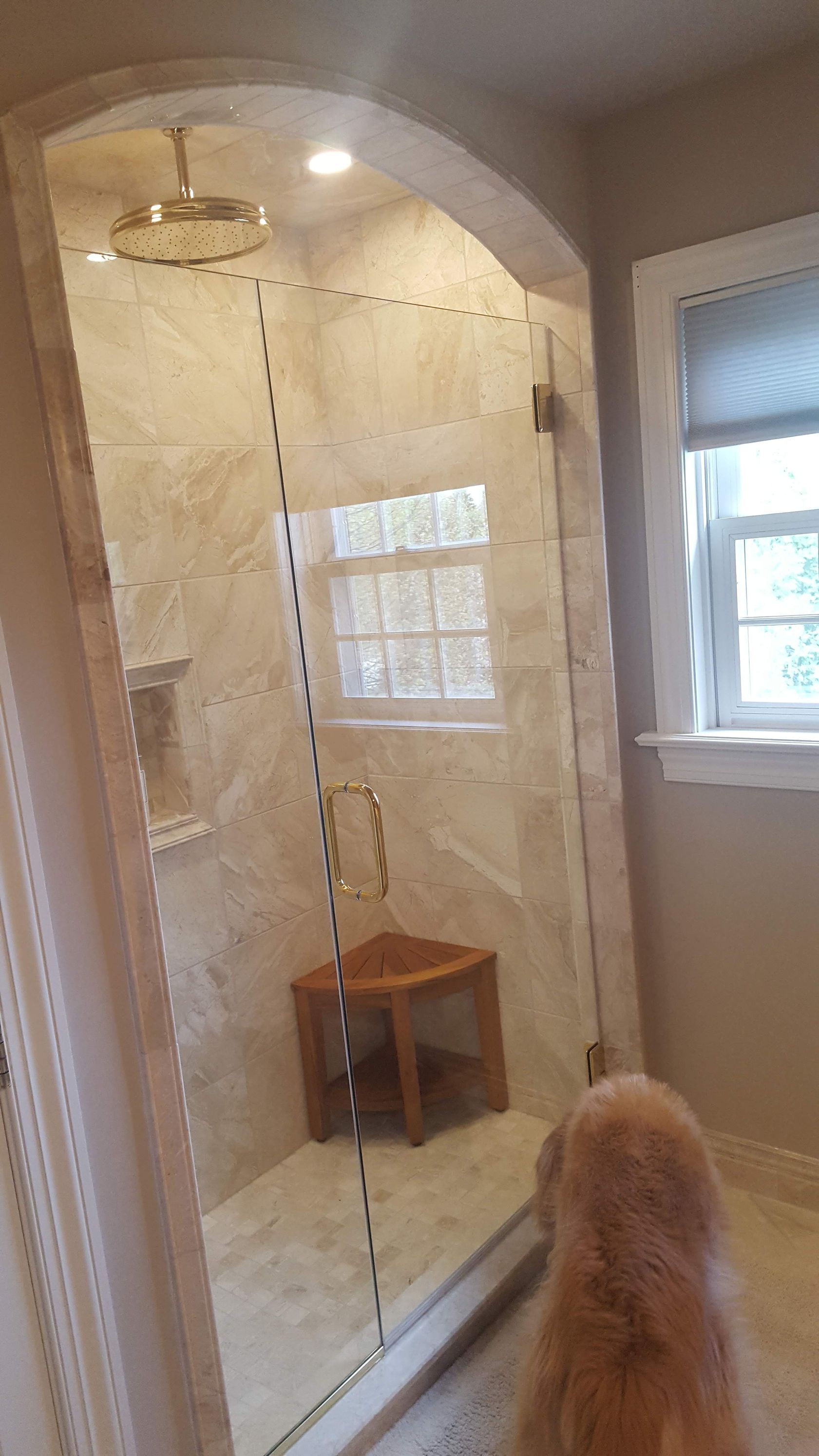 Bathroom with tiled walk-in shower, glass doors, small stool, and a window.