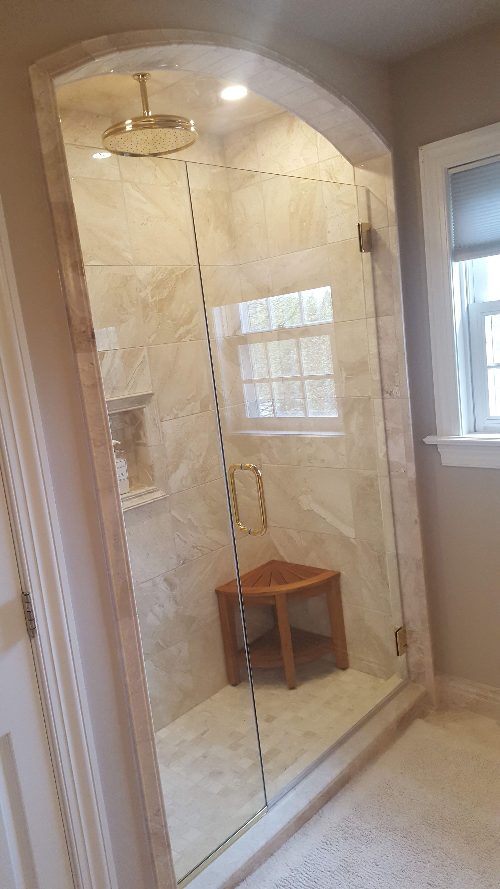 Frameless glass shower enclosure with gold trim in a beige tiled bathroom