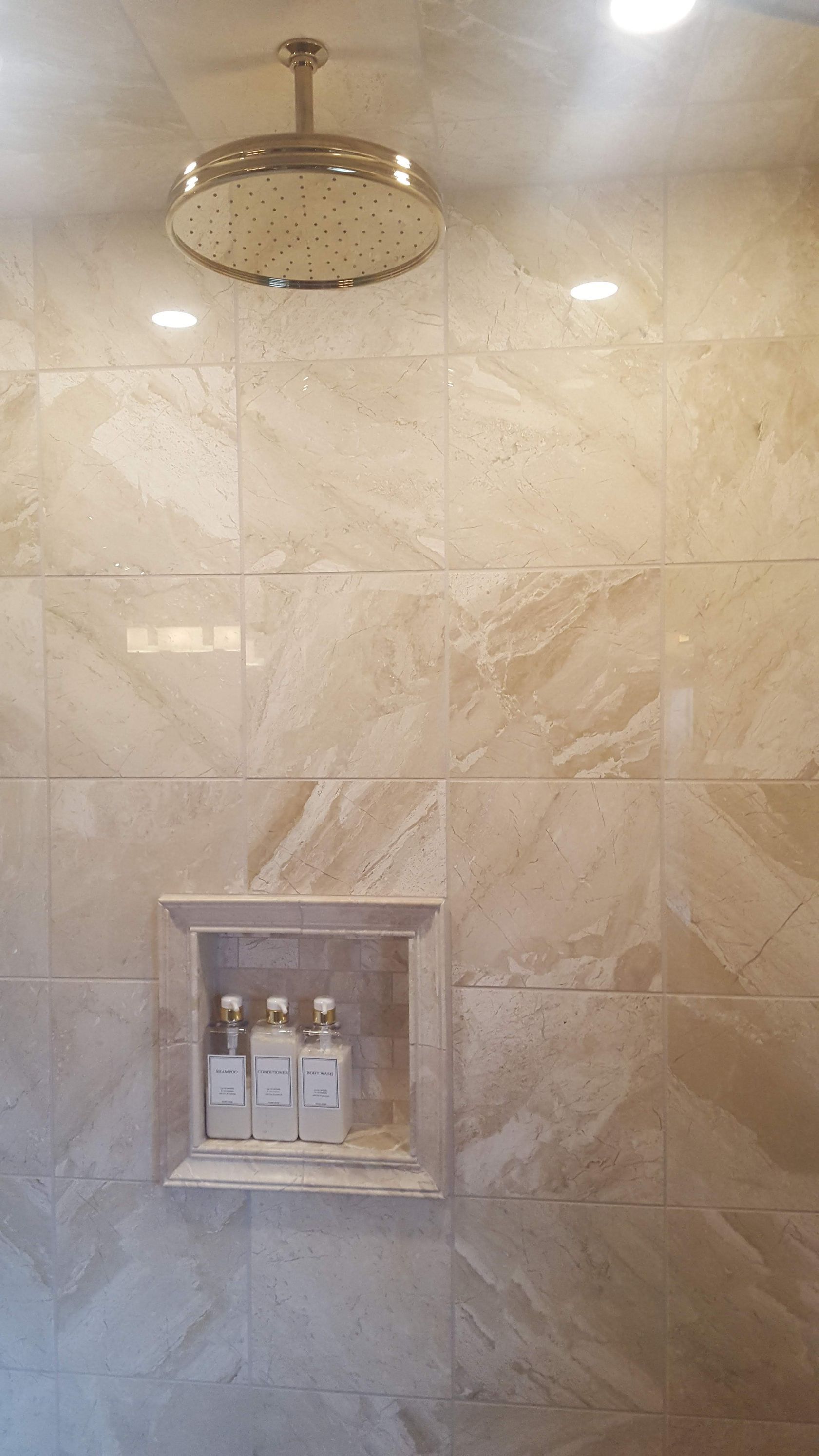 Marble-tiled shower wall with a round rainfall showerhead and built-in niche holding toiletries