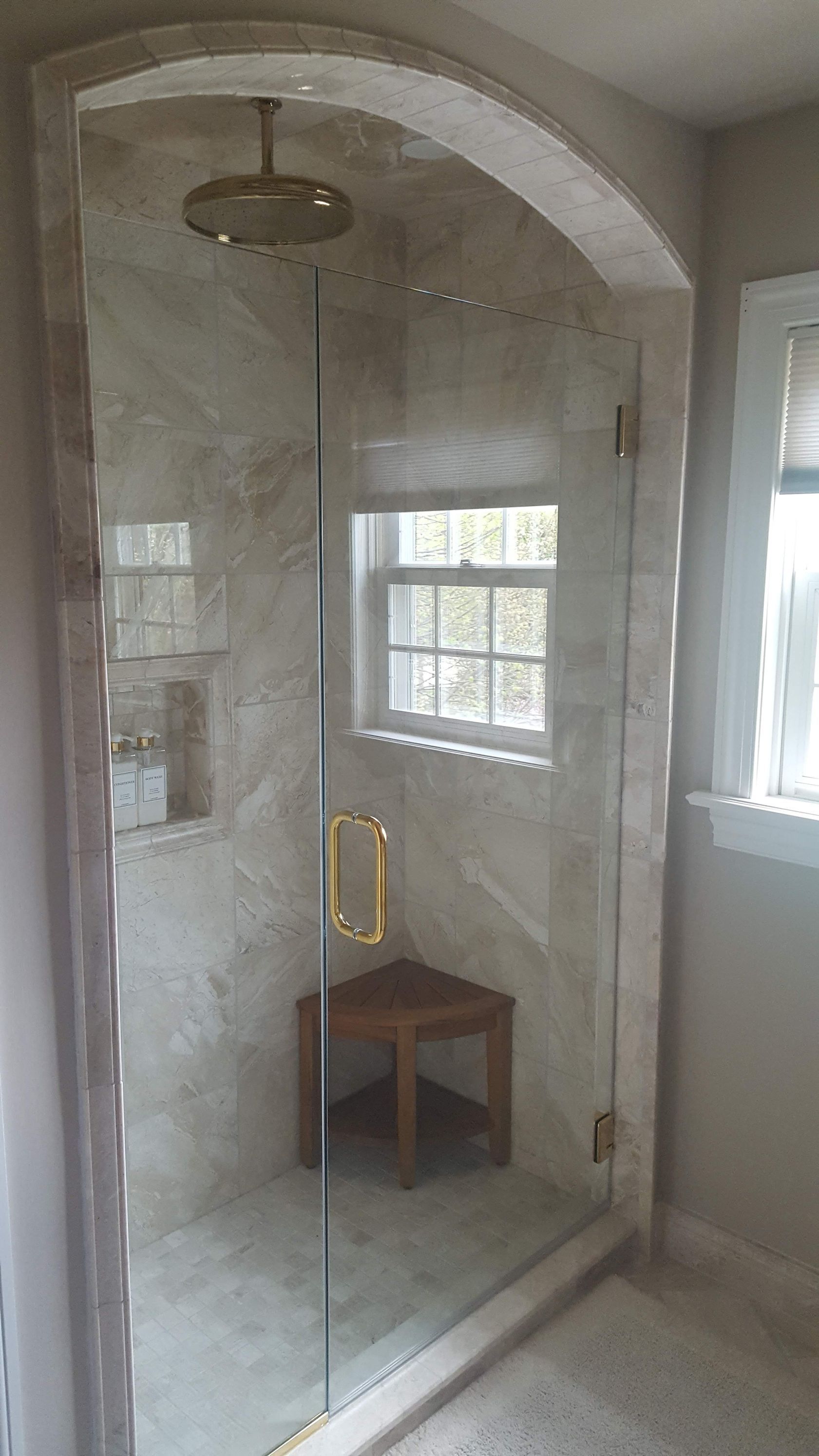 Glass shower enclosure with a tiled interior, arched opening, and a small stool inside.