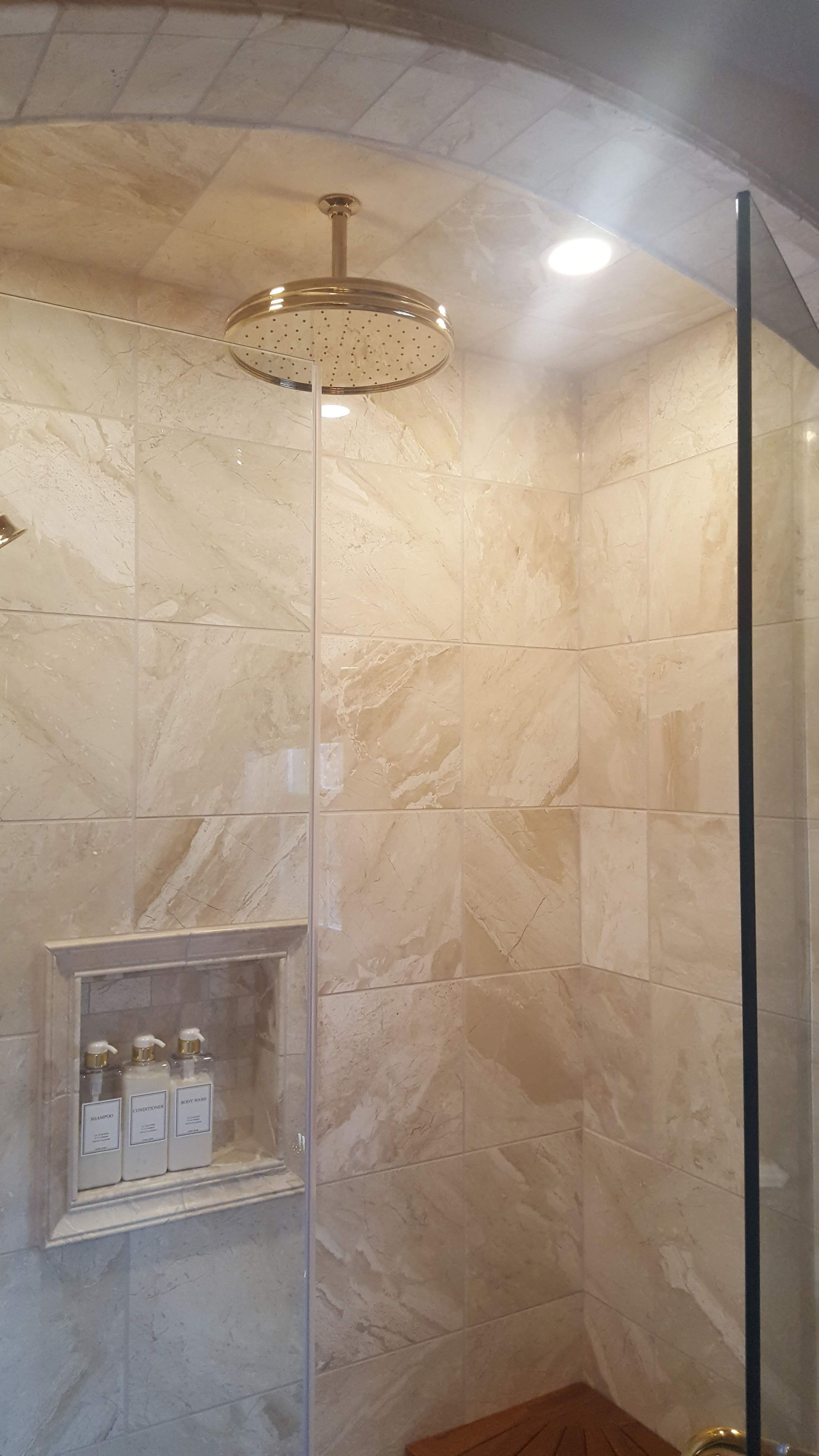 Tiled shower stall with a ceiling rain showerhead and built-in niche holding toiletries.