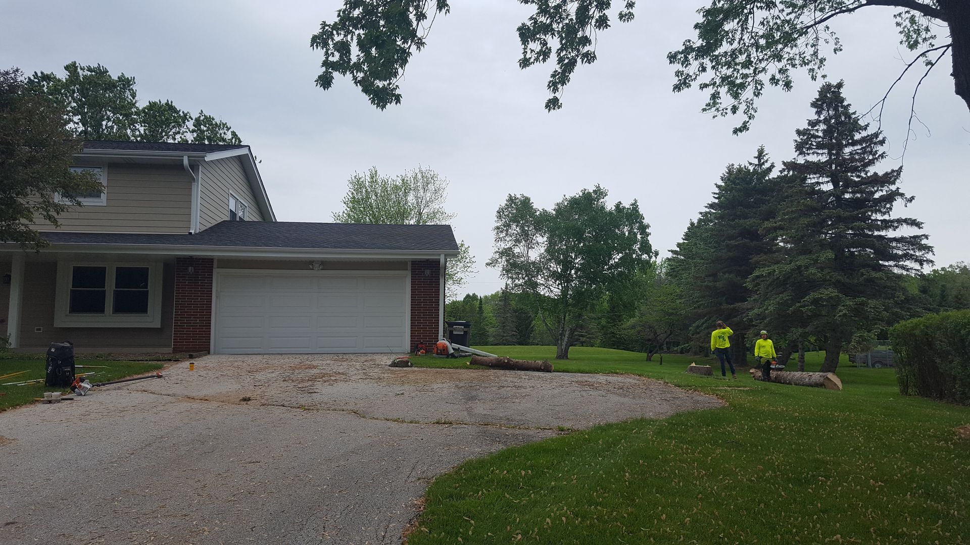 Suburban house with a garage, gravel driveway, and green lawn under cloudy skies