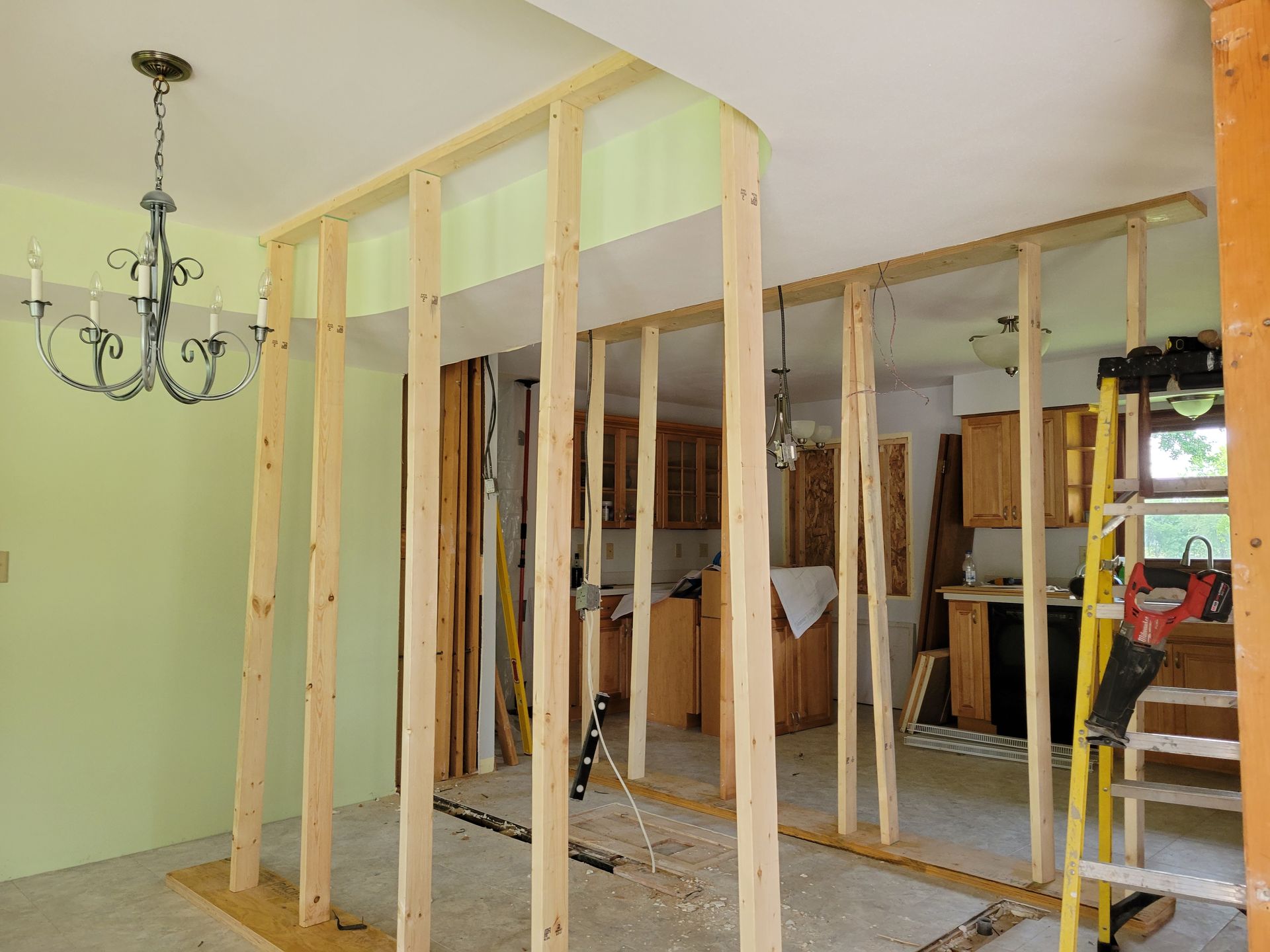 Partially framed room interior with exposed studs, chandelier, and ladder