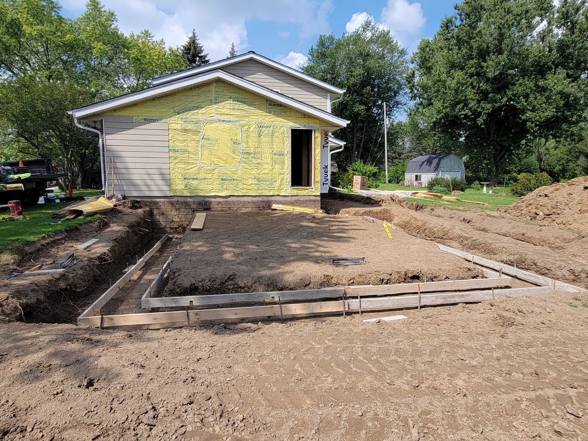 Partially built house with yellow sheathing and a dirt foundation site under construction