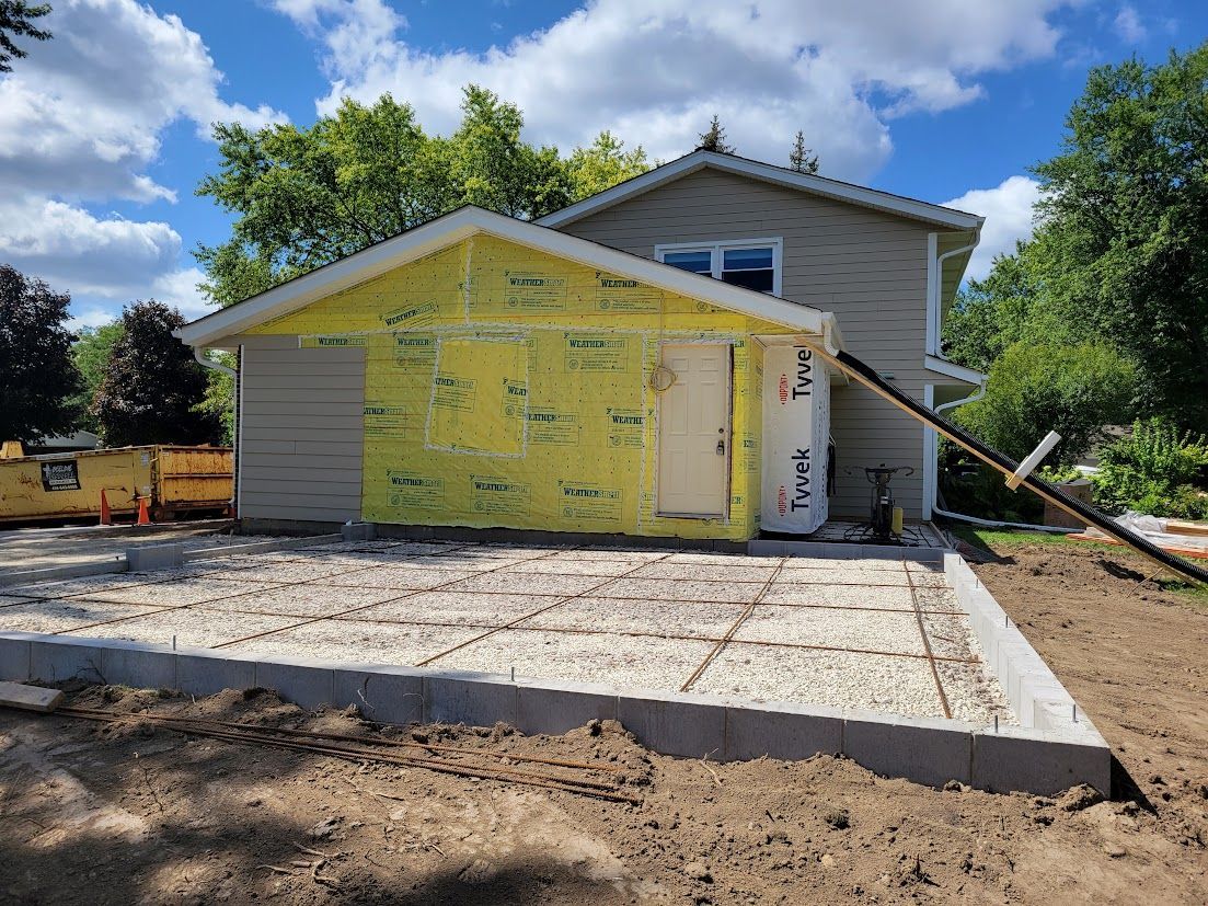 House under construction with yellow siding, white trim, and a concrete driveway under a partly cloudy sky