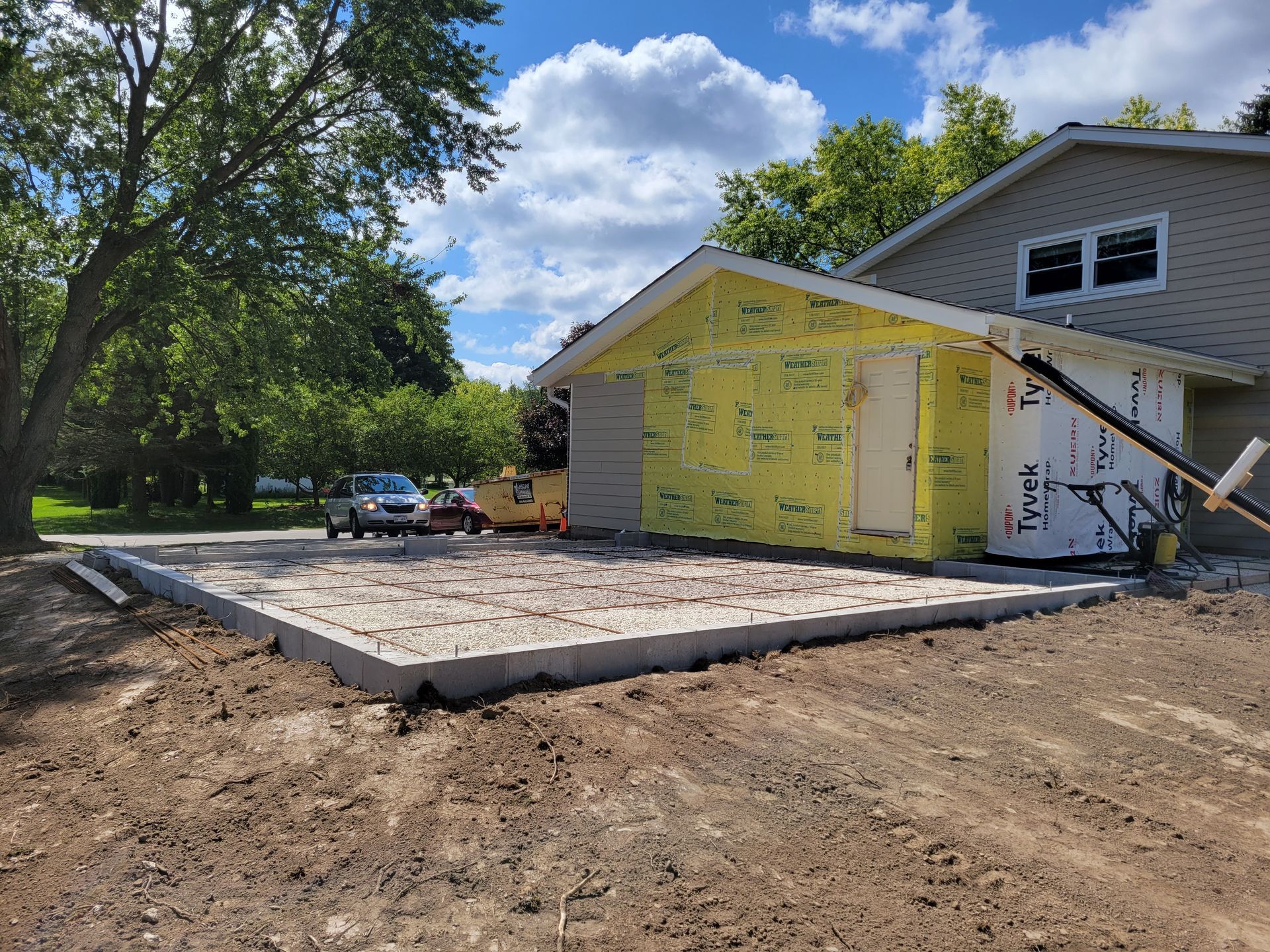 House under renovation with yellow insulation, new concrete patio, and dirt foreground
