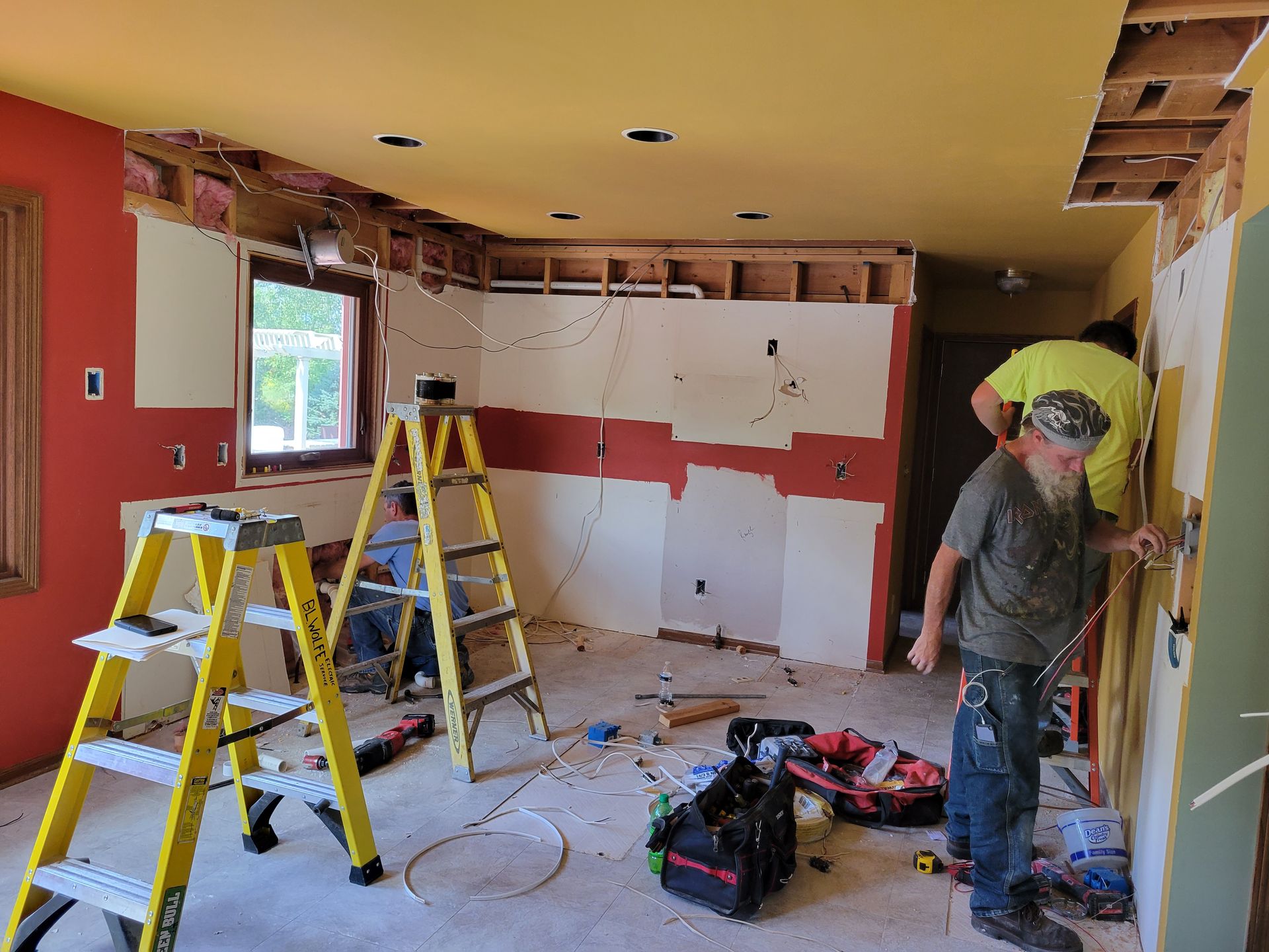 Home interior under renovation with ladders, tools, and a worker near a yellow tarp-covered doorway