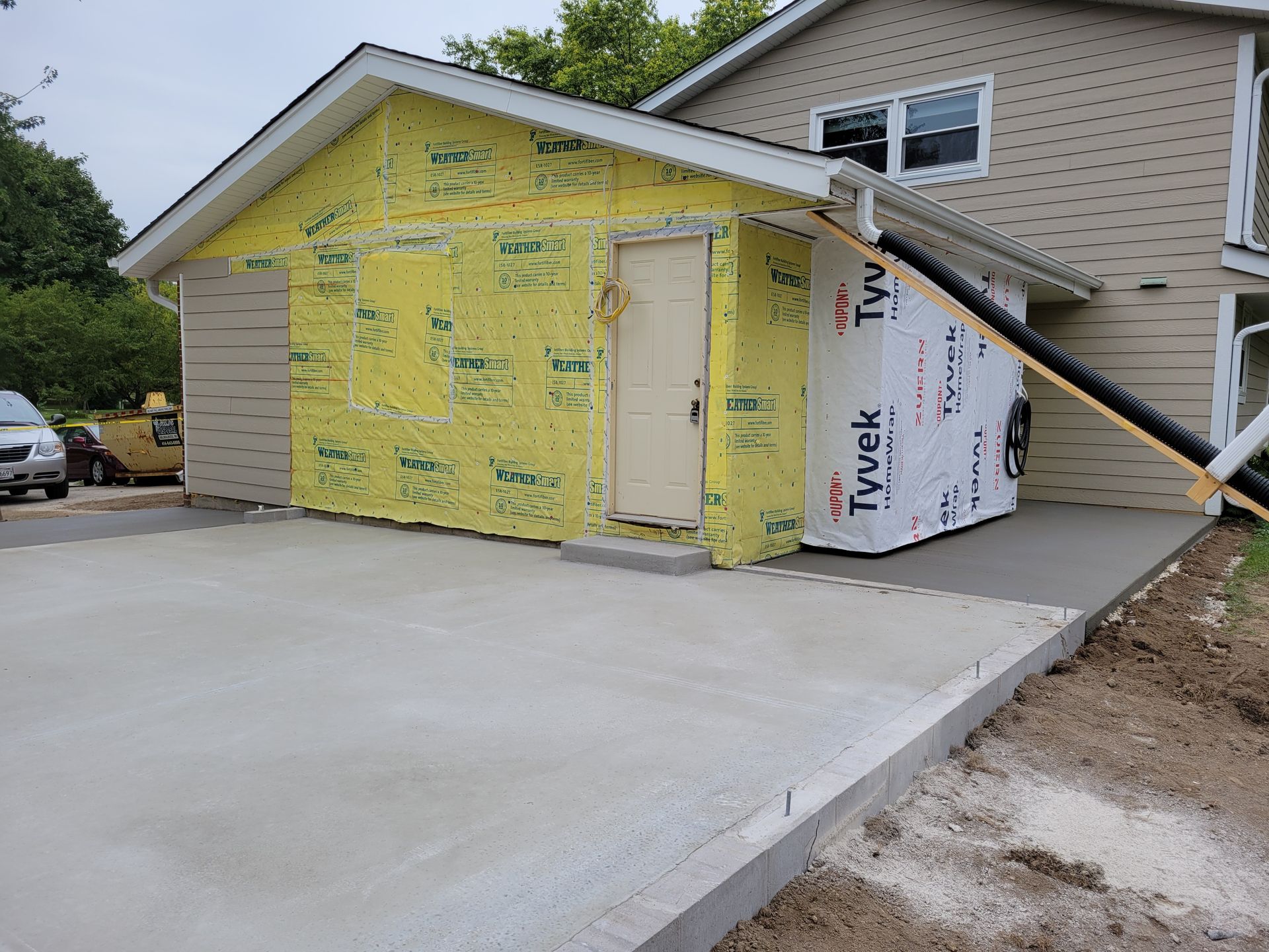House exterior under construction with yellow and white house wrap and a concrete driveway.