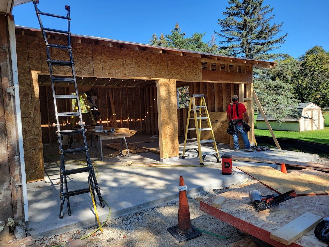 Workers renovating a building exterior with ladders, exposed framing, and construction tools in daylight