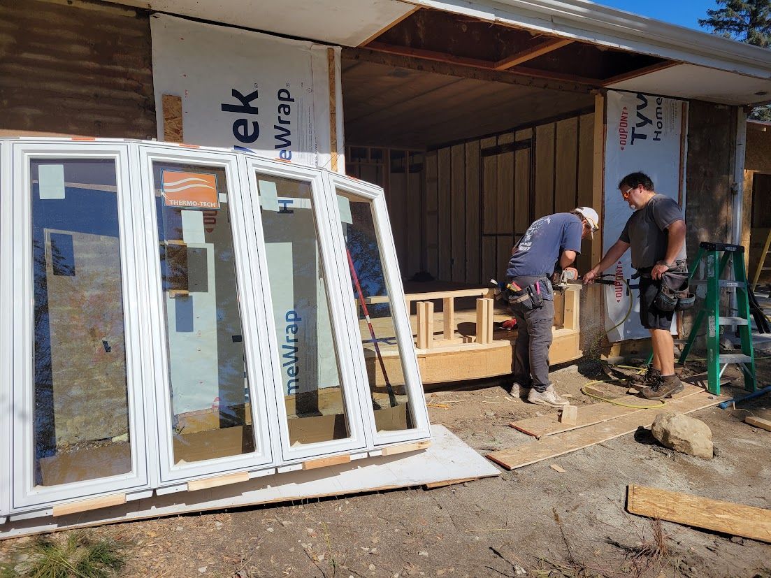 Two workers installing a large white door frame at a house under construction