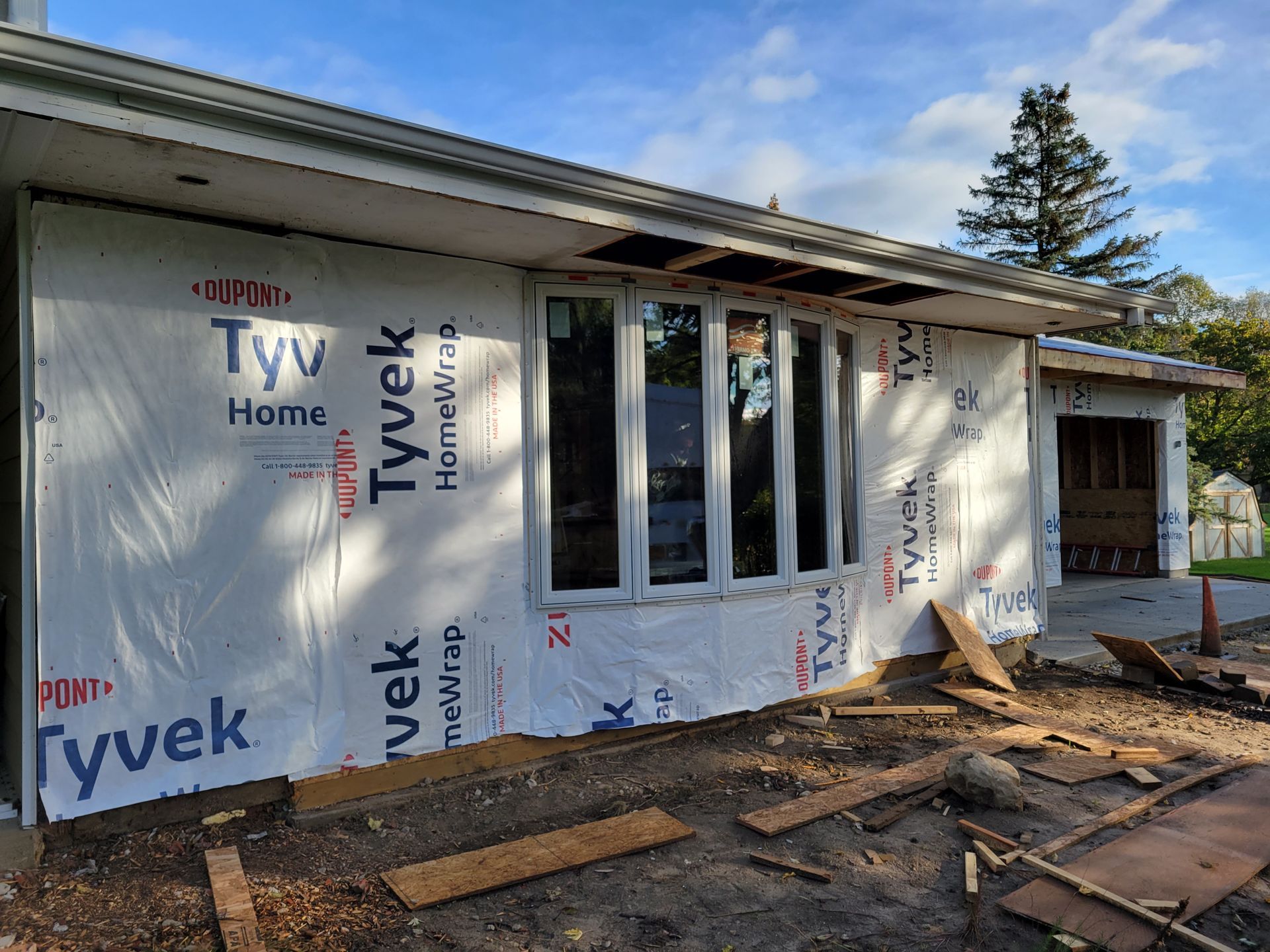 House under construction wrapped in Tyvek, with unfinished siding, windows, and debris in front