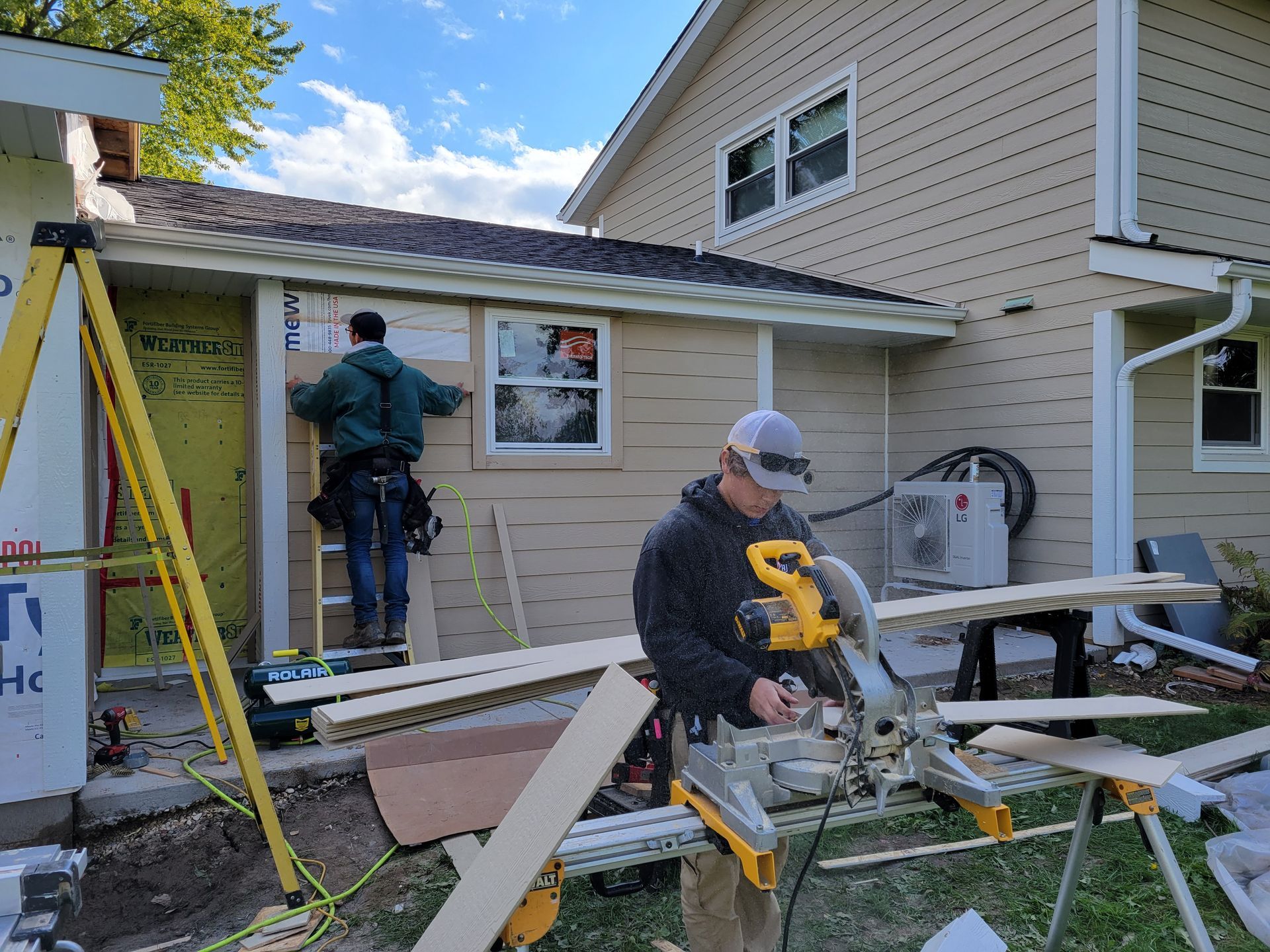 Workers cutting lumber outside a beige house during home renovation.