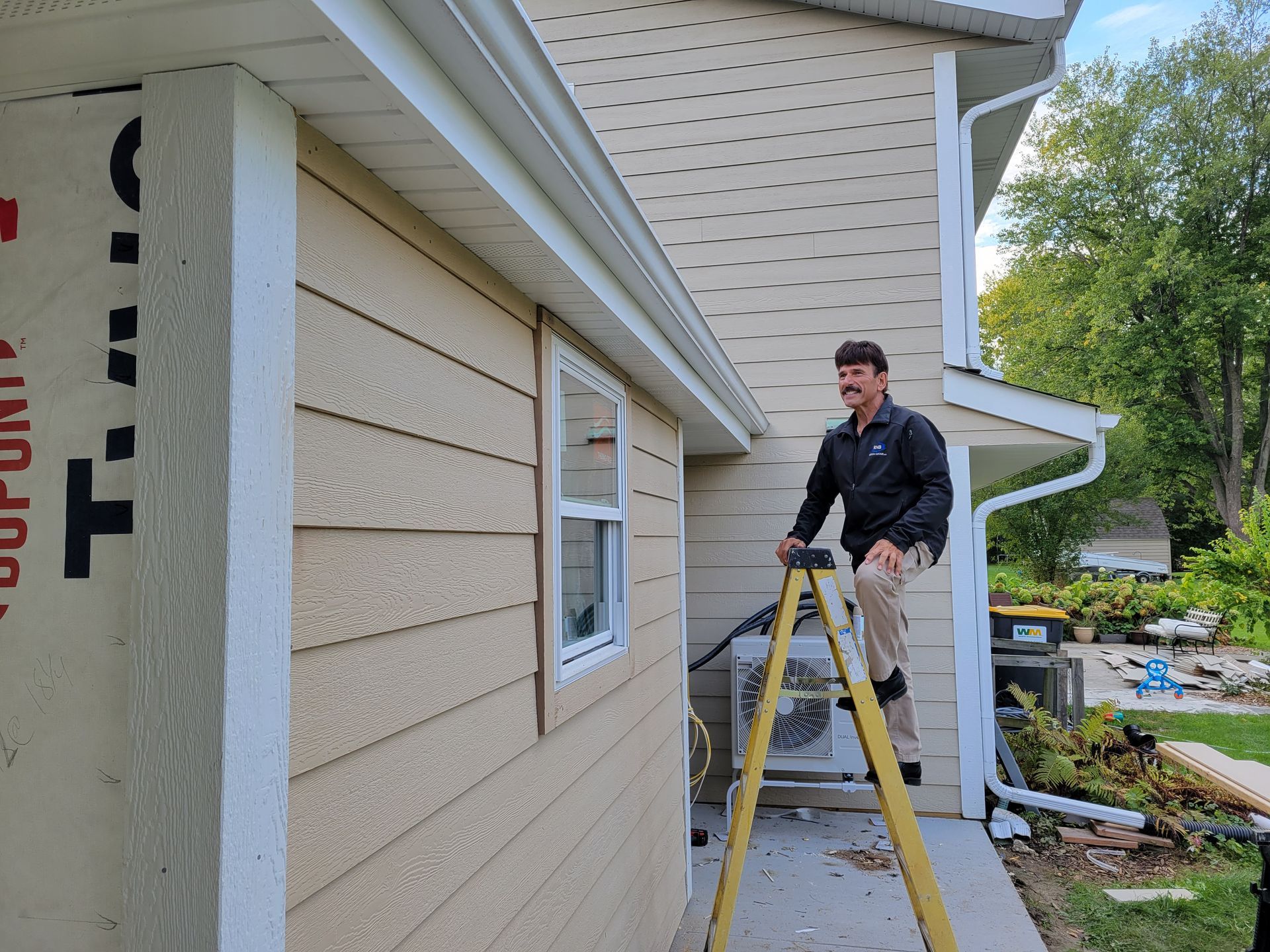 Person on a step ladder painting beige siding on a house exterior.