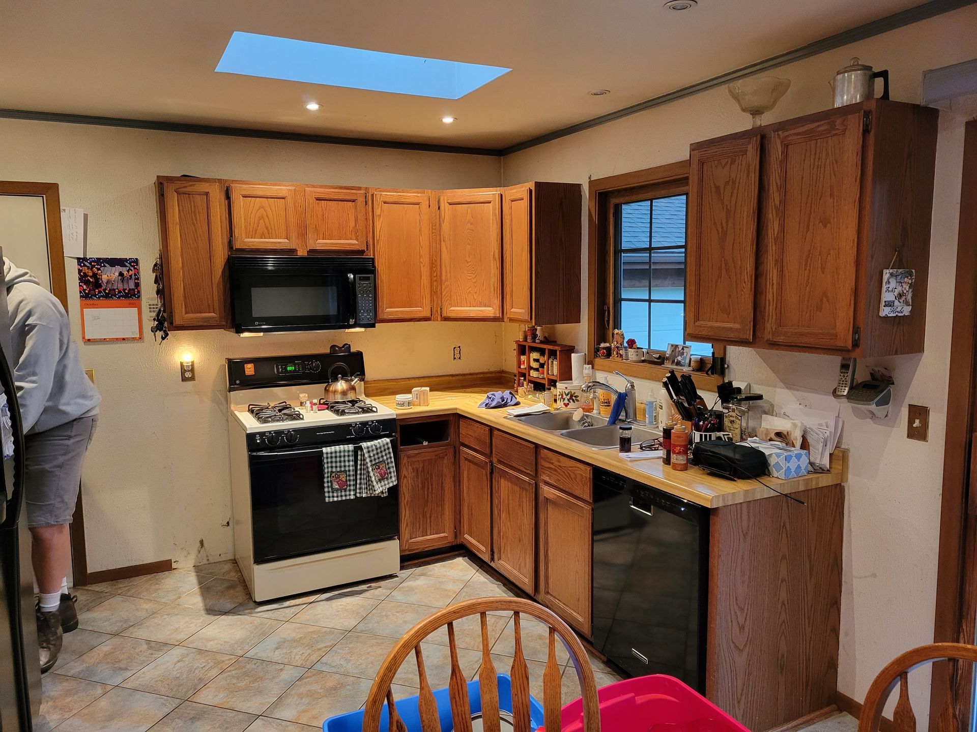 Kitchen with wooden cabinets, black appliances, tiled floor, and a skylight above the counter.