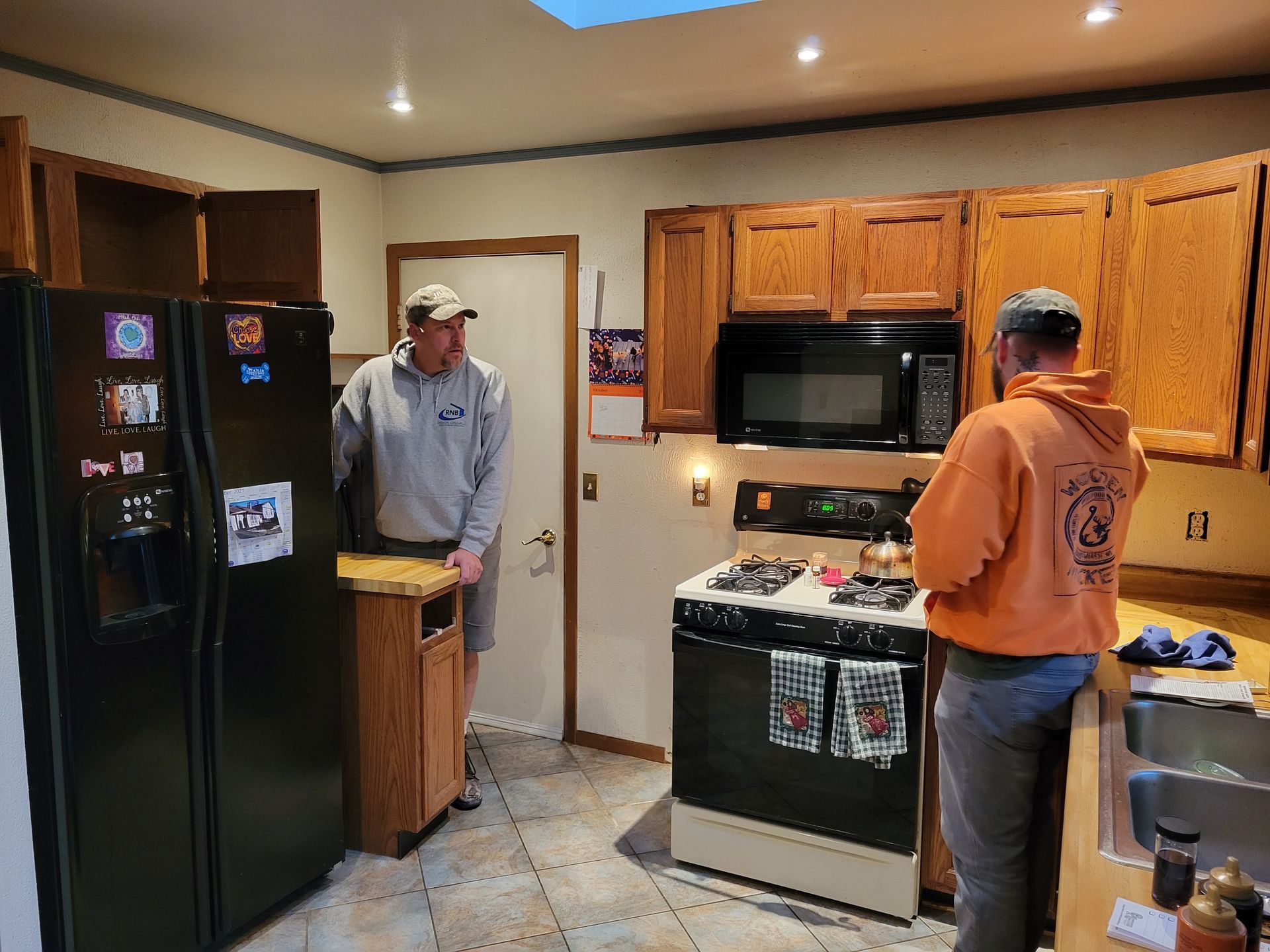 Two men standing in a kitchen with black appliances and wooden cabinets