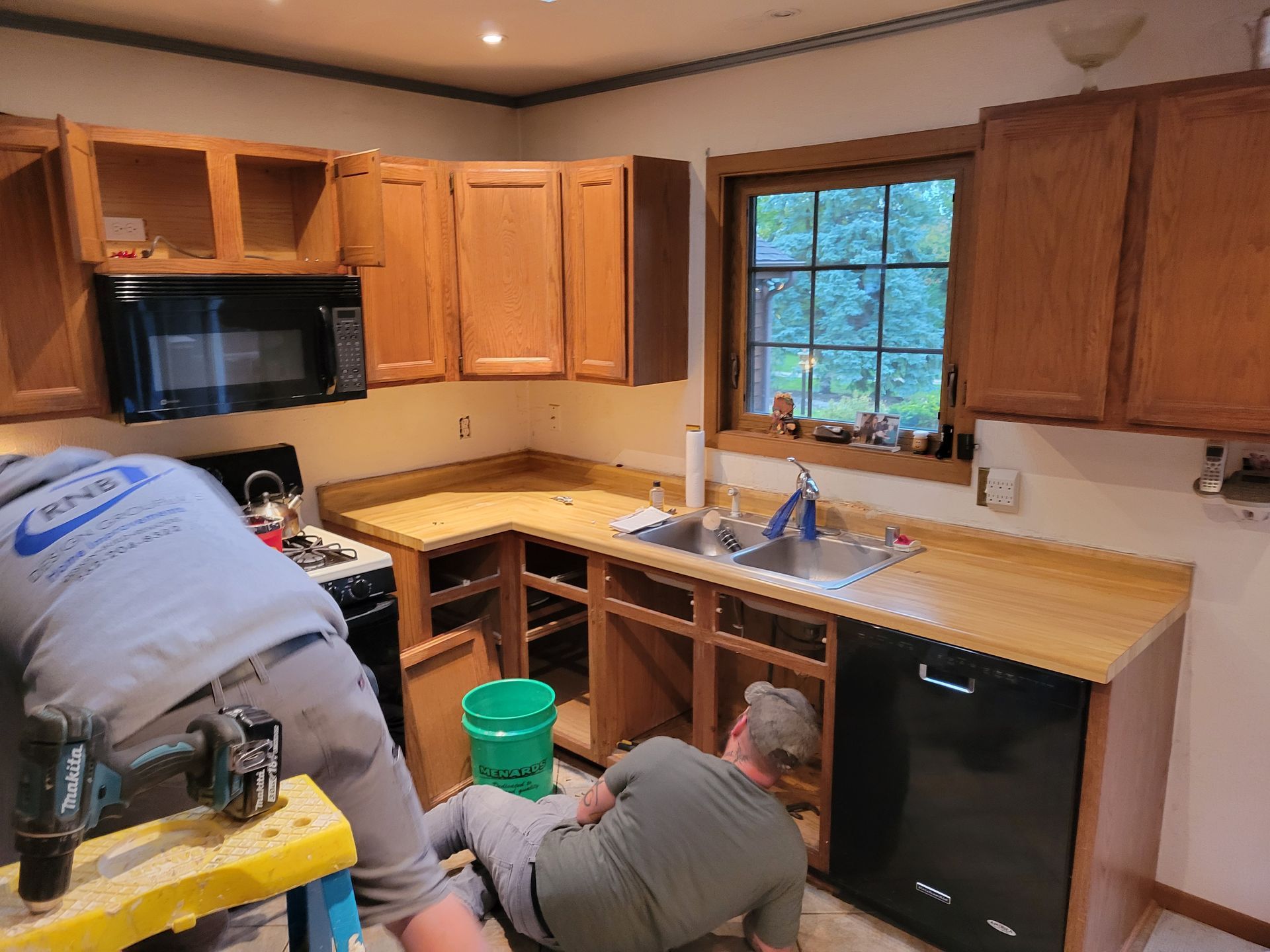 Two workers installing cabinets and a sink in a kitchen under renovation