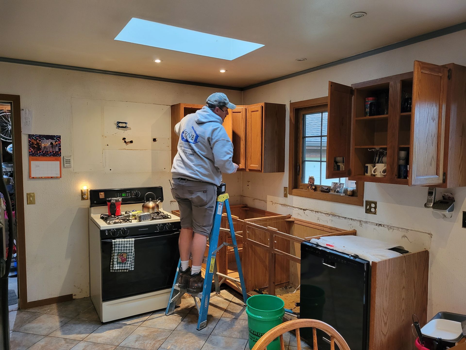 Person on a ladder working on kitchen cabinets in a partially renovated kitchen