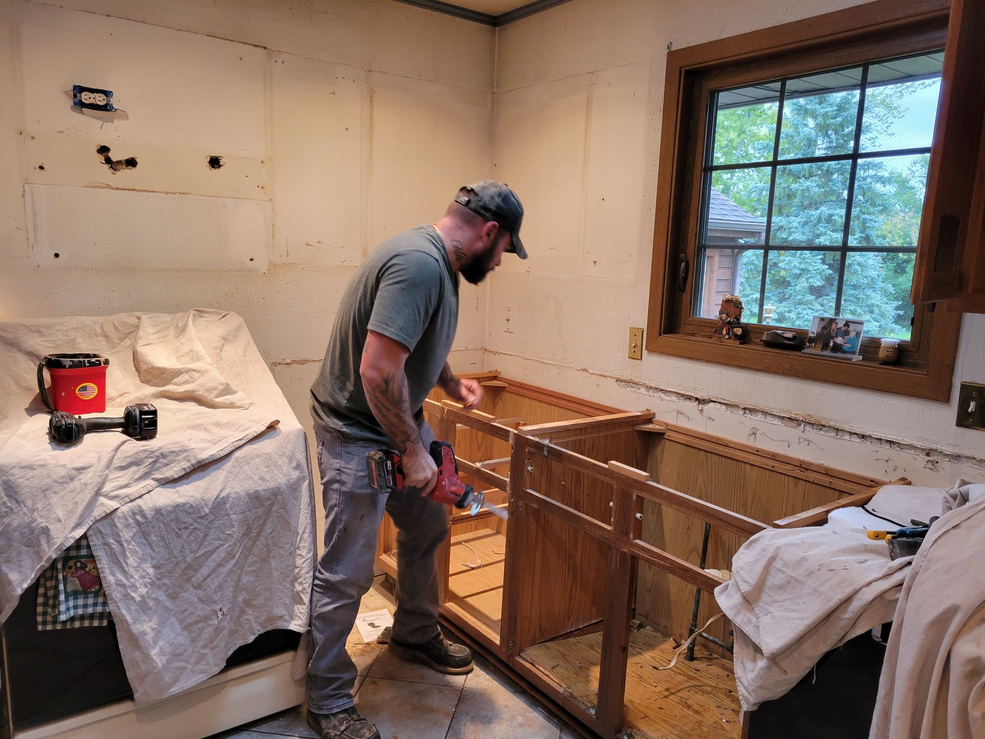 Person working on a kitchen renovation beside exposed cabinets and a window.